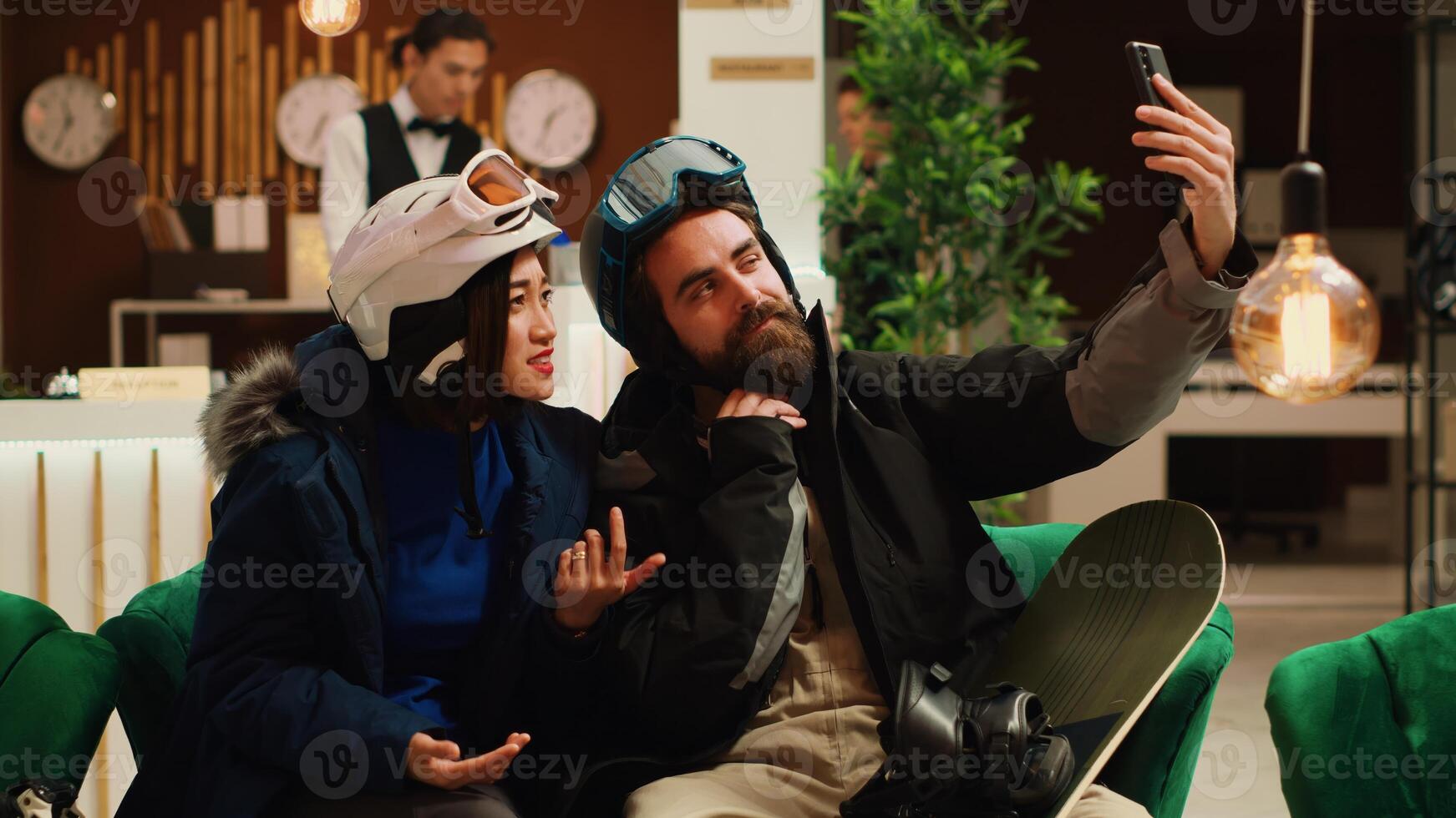 Travellers answer videocall at hotel, waving at friends calling on online teleconference connection. Man and woman talking to people remotely while on ski resort winter vacation. Handheld shot. photo