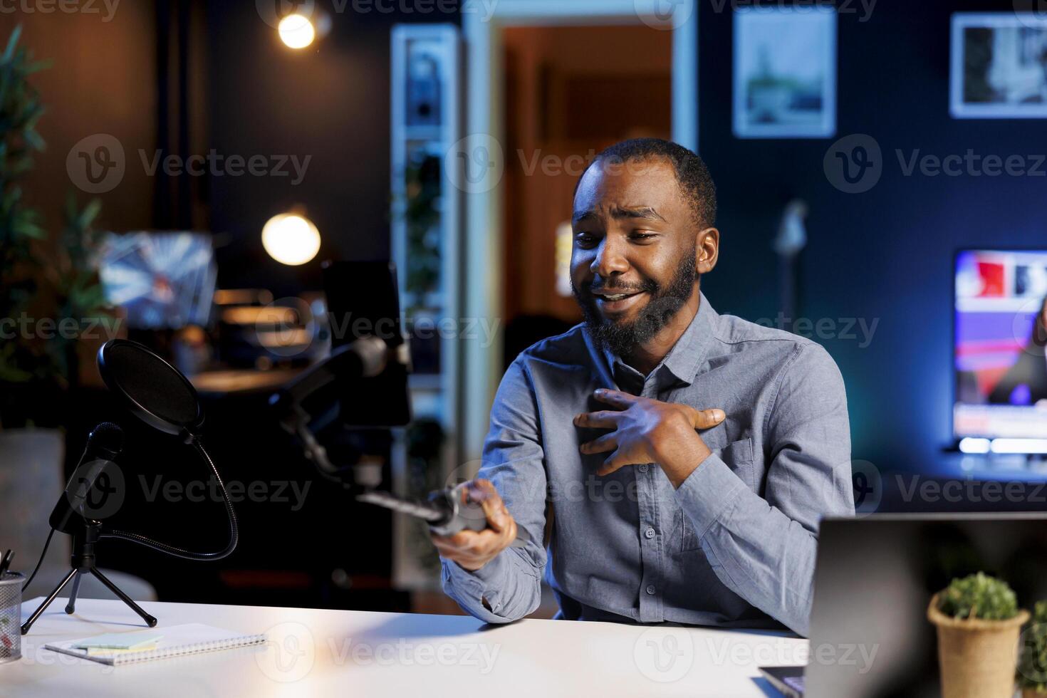 African american internet show host in blurry background hitting the record button on smartphone. Mobile phone attached to selfie stick used by media star to record footage for viewers photo