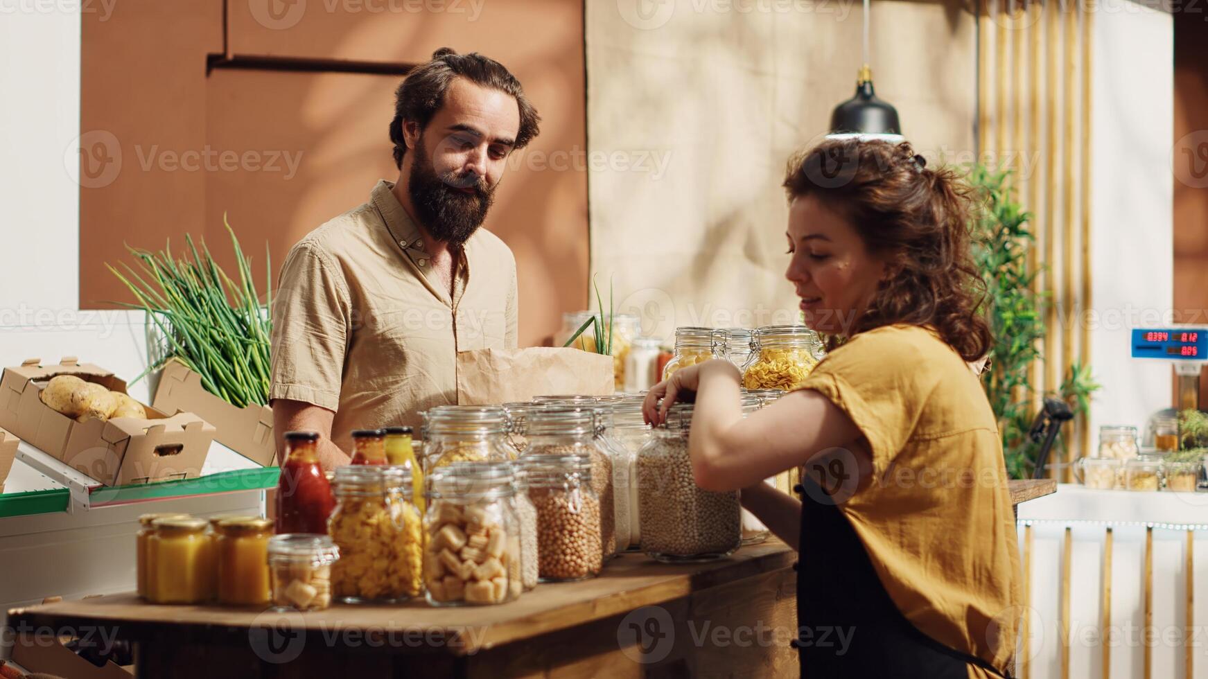Client talking with vendor in zero waste supermarket, inquiring about food items provenience, making sure they have ethical sourcing. Man in local store chatting with storekeeper about bulk products photo