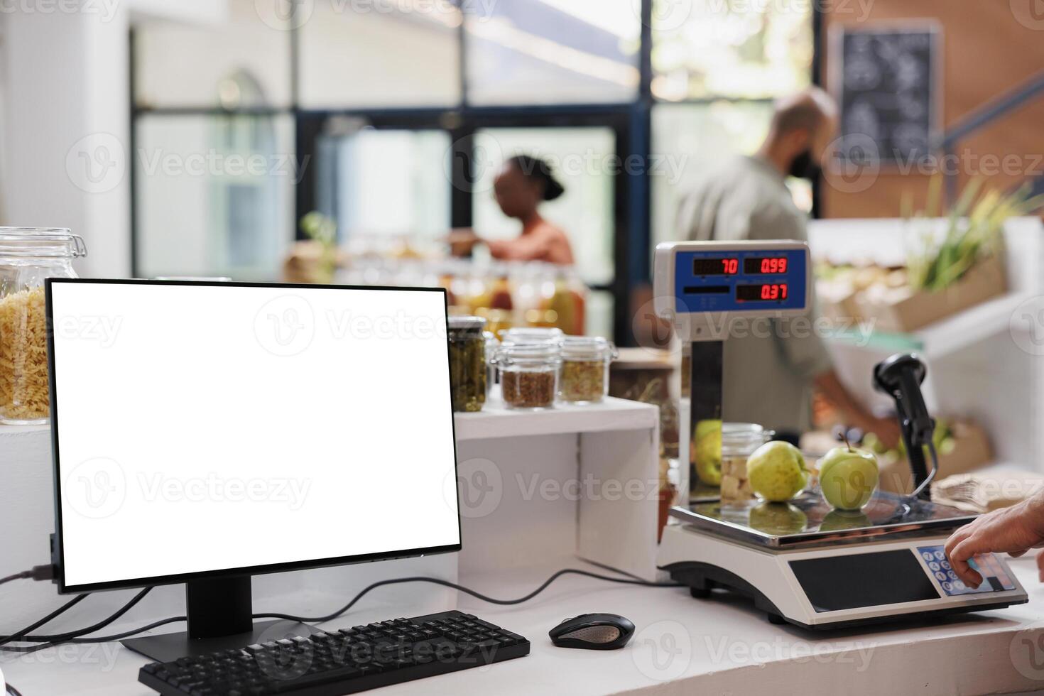 Desktop computer showing blank white screen while a salesperson measures apples using a weighing scale. Positioned at cashier desk is a pc monitor displaying isolated chromakey mockup template. photo