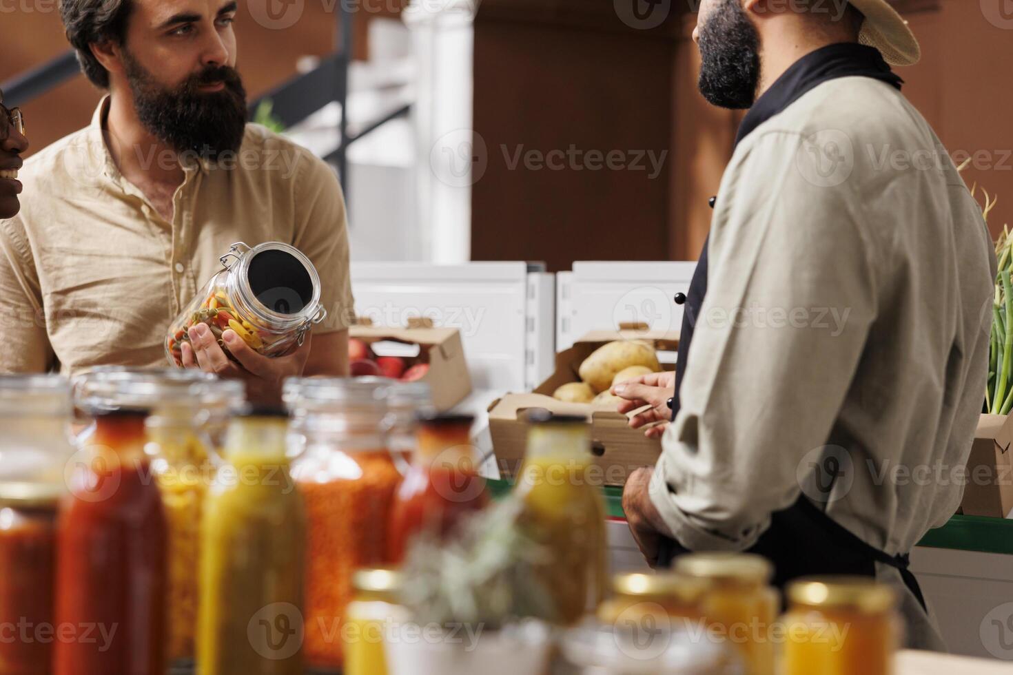 Close-up of eco friendly bulk product vendor sharing his homemade sauce and pasta bolognese recipe with a couple at supermarket. The zero waste store offers excellent customer service. photo