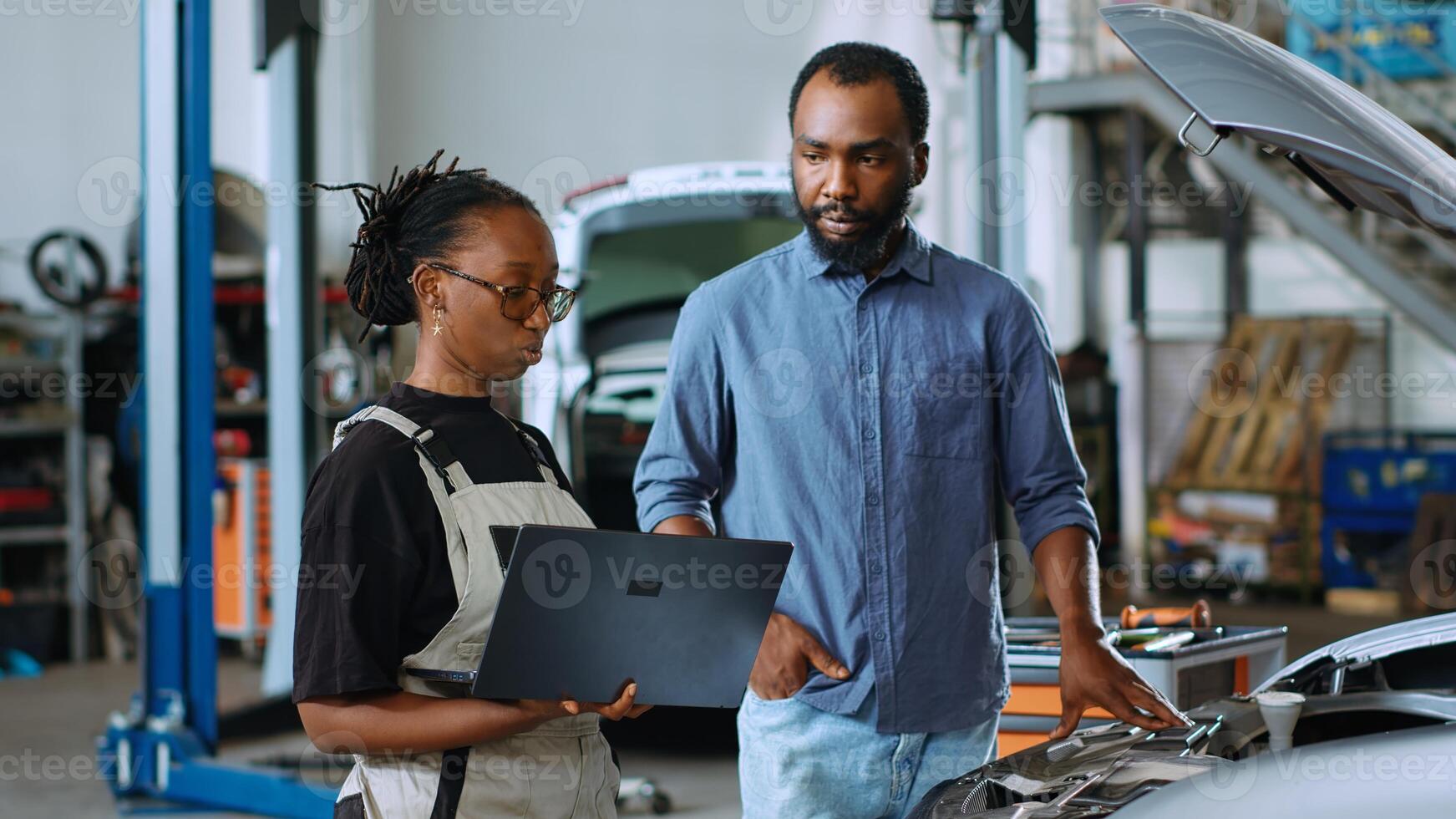 Precise mechanic in car service uses laptop to calculate repairments invoice for client after fixing broken parts. Trained expert using device to inform man of final costs after reconditioning vehicle photo