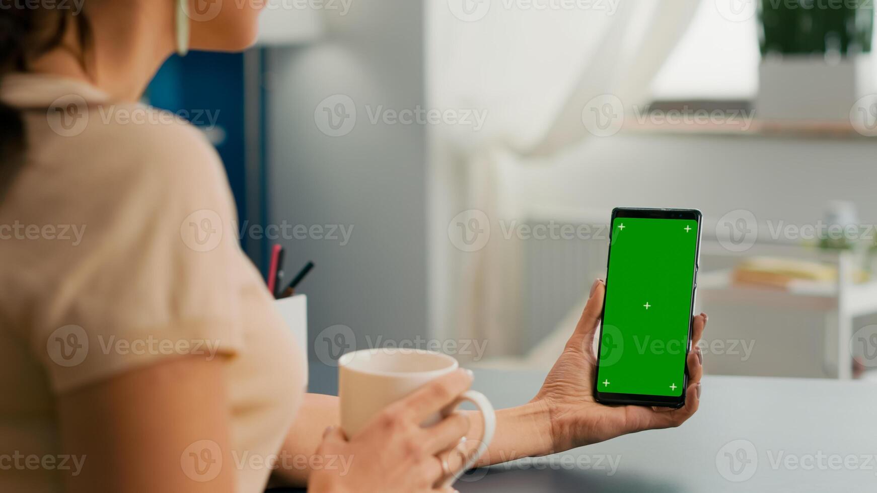 Caucasian female having online videocall using mock up green screen chroma key phone. Business woman working at online app using isolated device siiting on office desk in home office photo