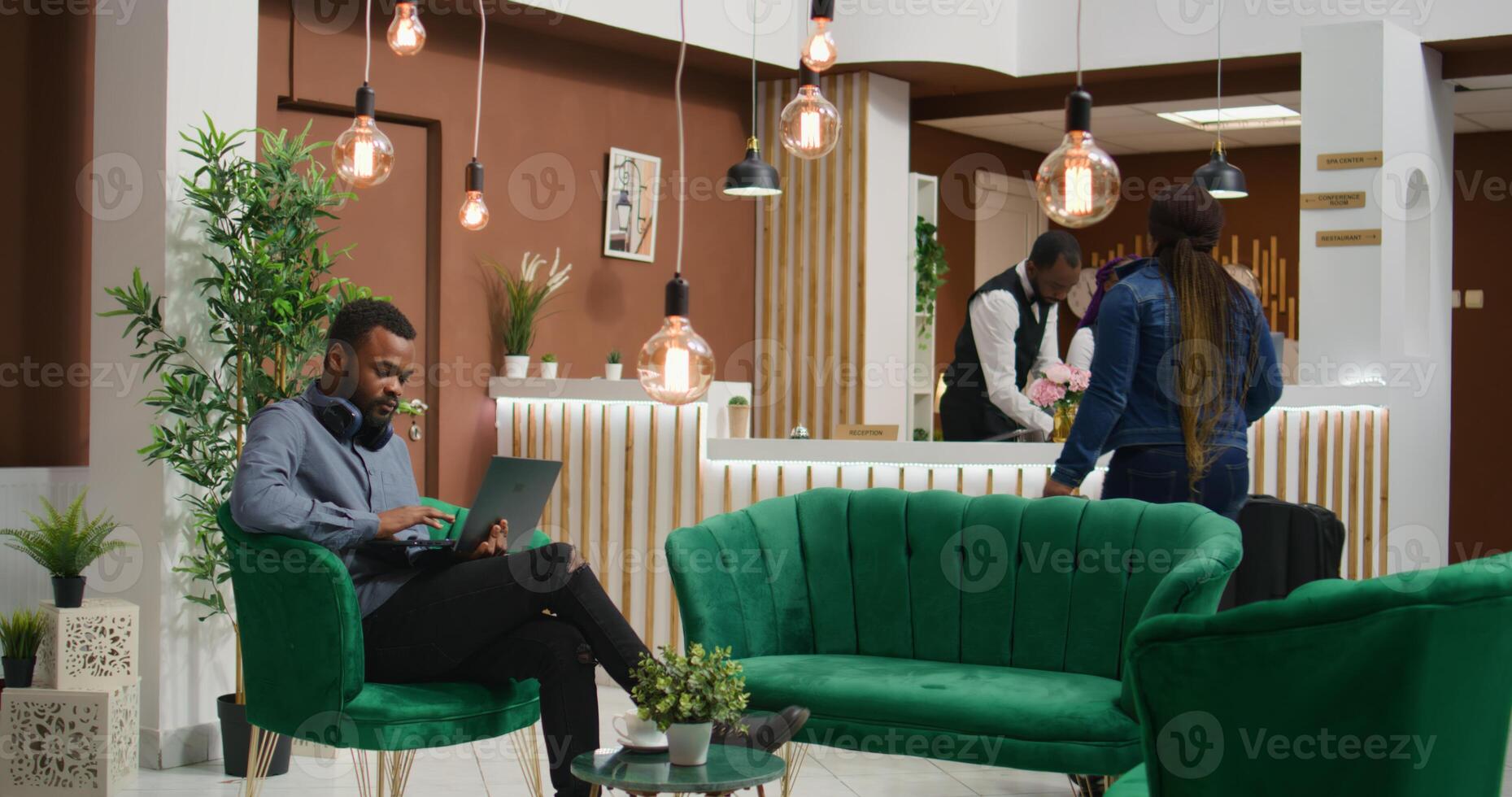Traveller browsing social media at hotel, relaxing in lounge area with laptop before signing check in papers. African american person arriving at holiday resort, using computer on vacation. photo