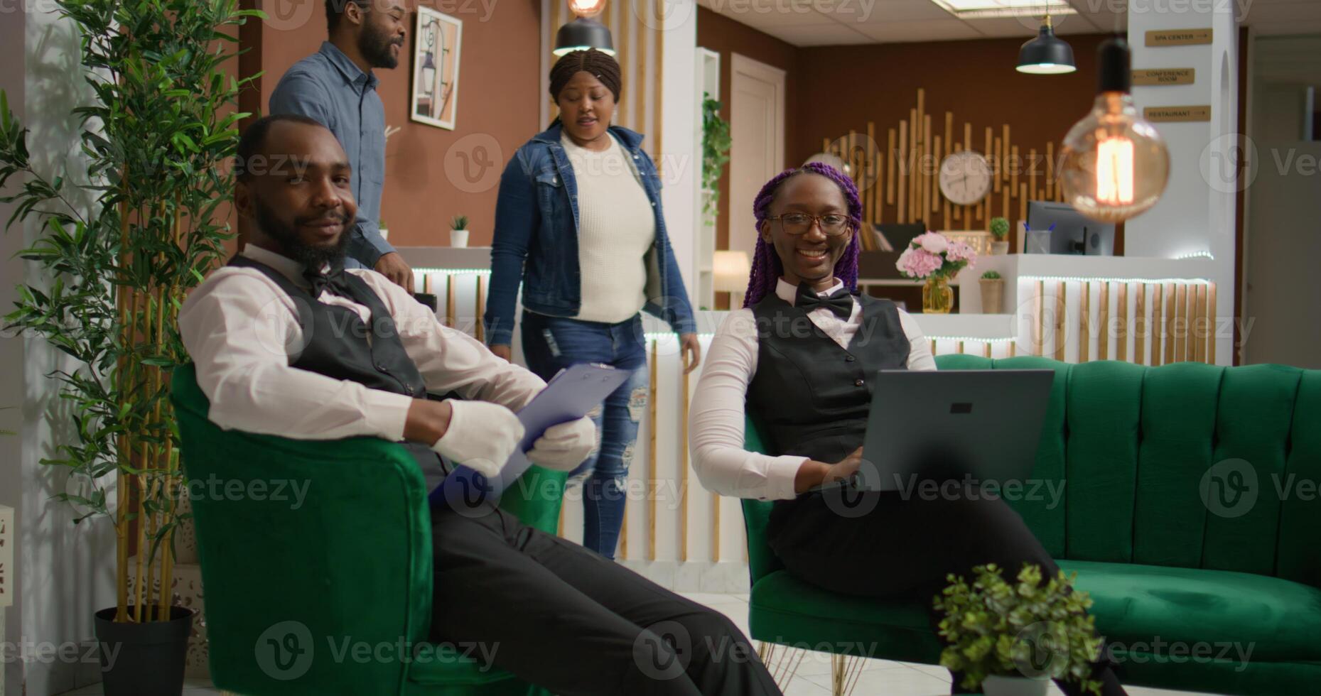 Employees of hotel checking information on papers and laptop, creating list of rooms for guests at reception lobby. At five star retreat, team of bellboy and receptionist oversee reservations. photo