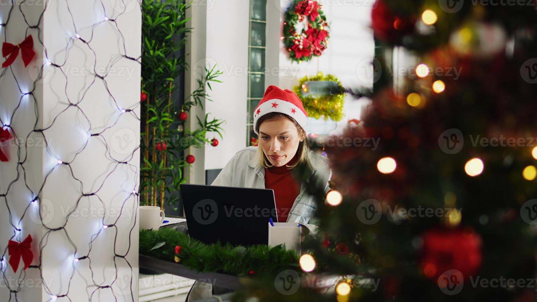 Zoom in shot on focused employee working on overdue project during Christmas season in festive decorated office. Worker in multicultural workplace adorn with red xmas garlands and bows photo