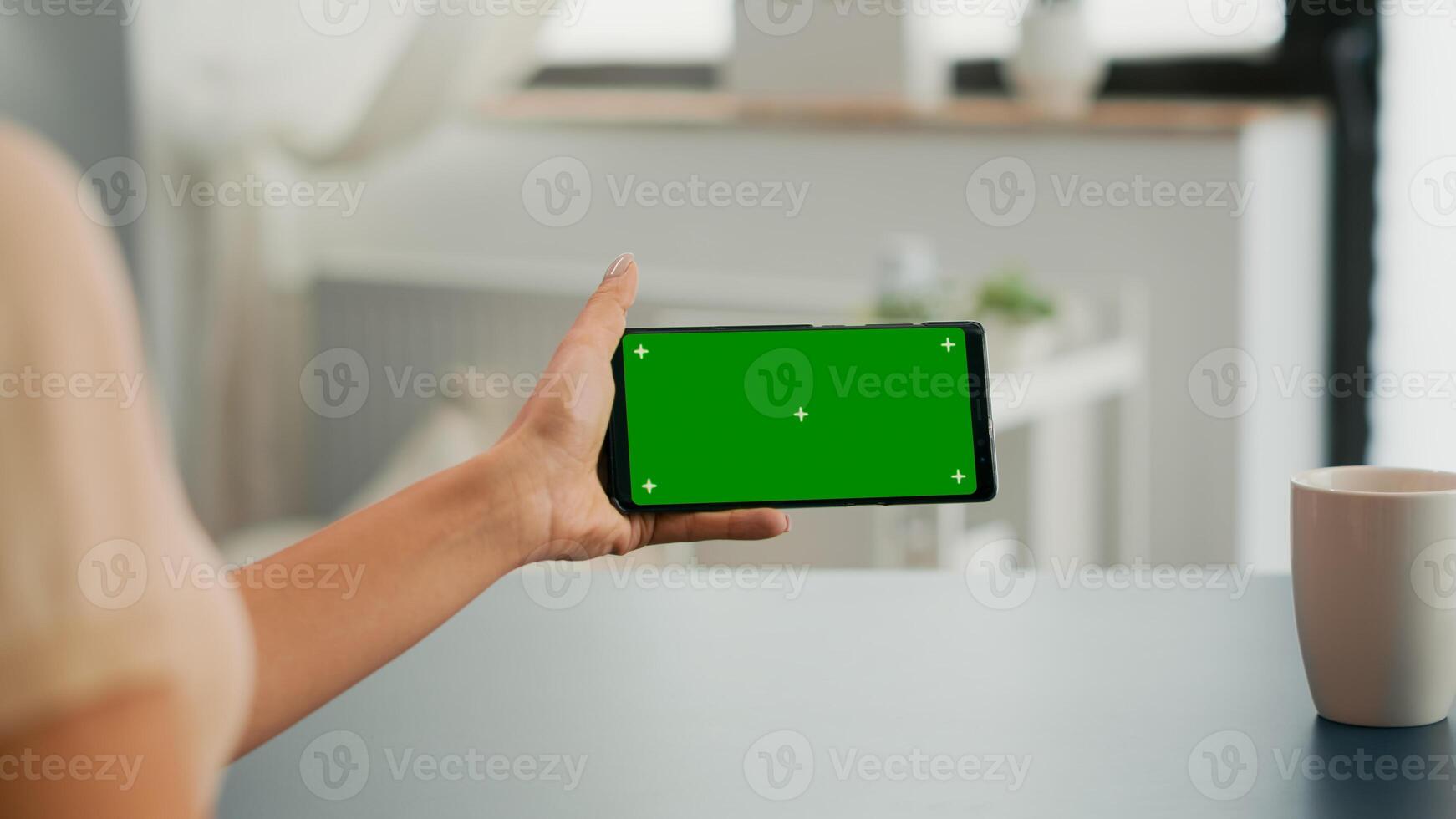 Freelancer holding smartphone with mock up green screen chroma key in horizontal position. Business woman searching online information using isolated device sitting on office desk photo