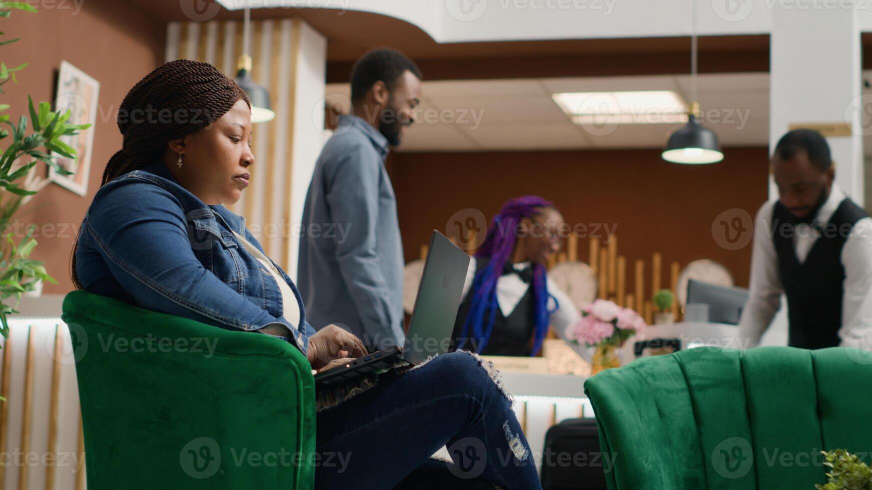 Traveller sitting in lobby with laptop, using online website before registering at reception front desk. Woman tourist working on portable pc in lounge area, holiday accommodation. Handheld shot. photo