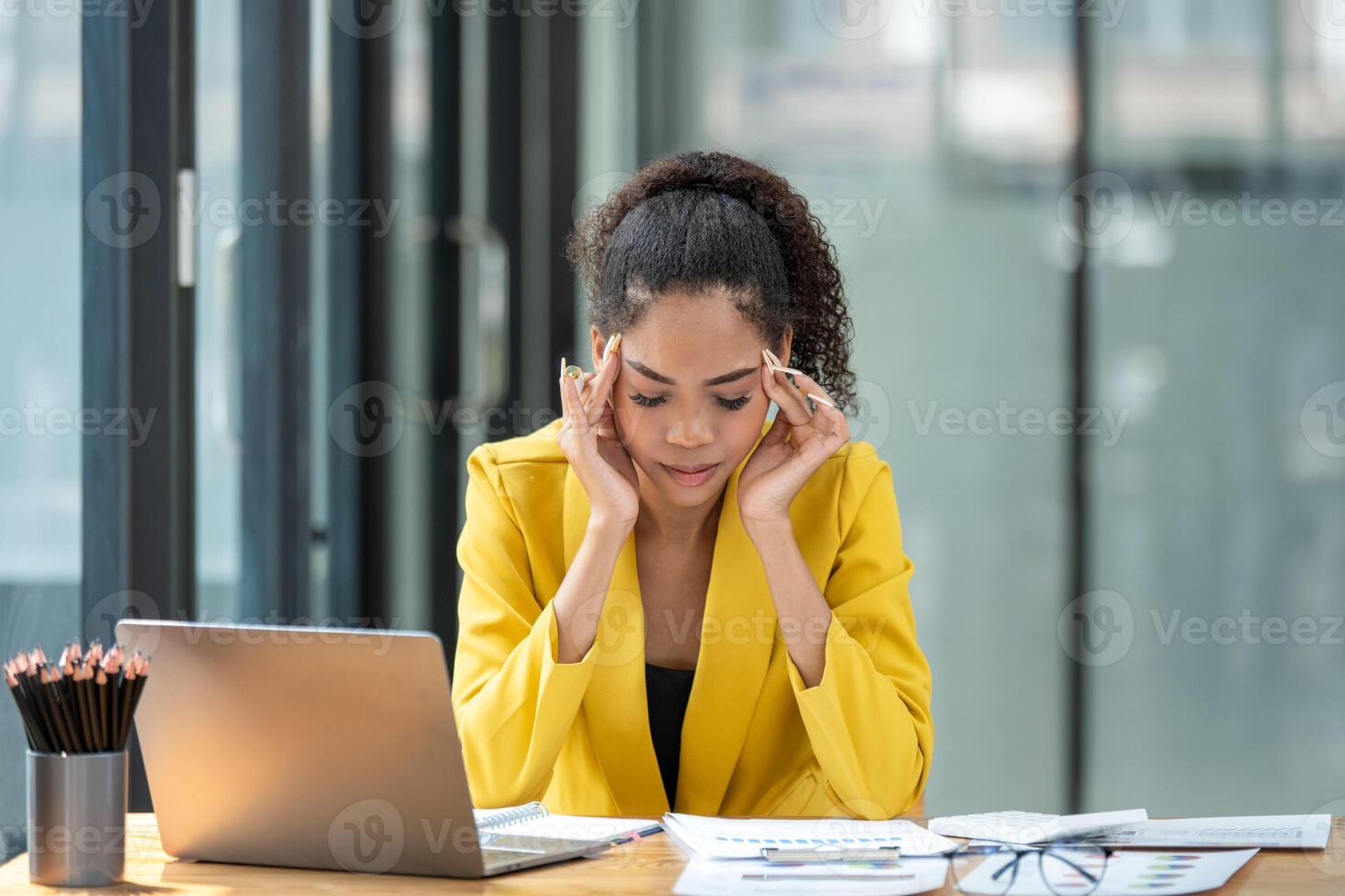Distressed young businesswoman feeling pressure and headache at her office desk with laptop and documents. photo