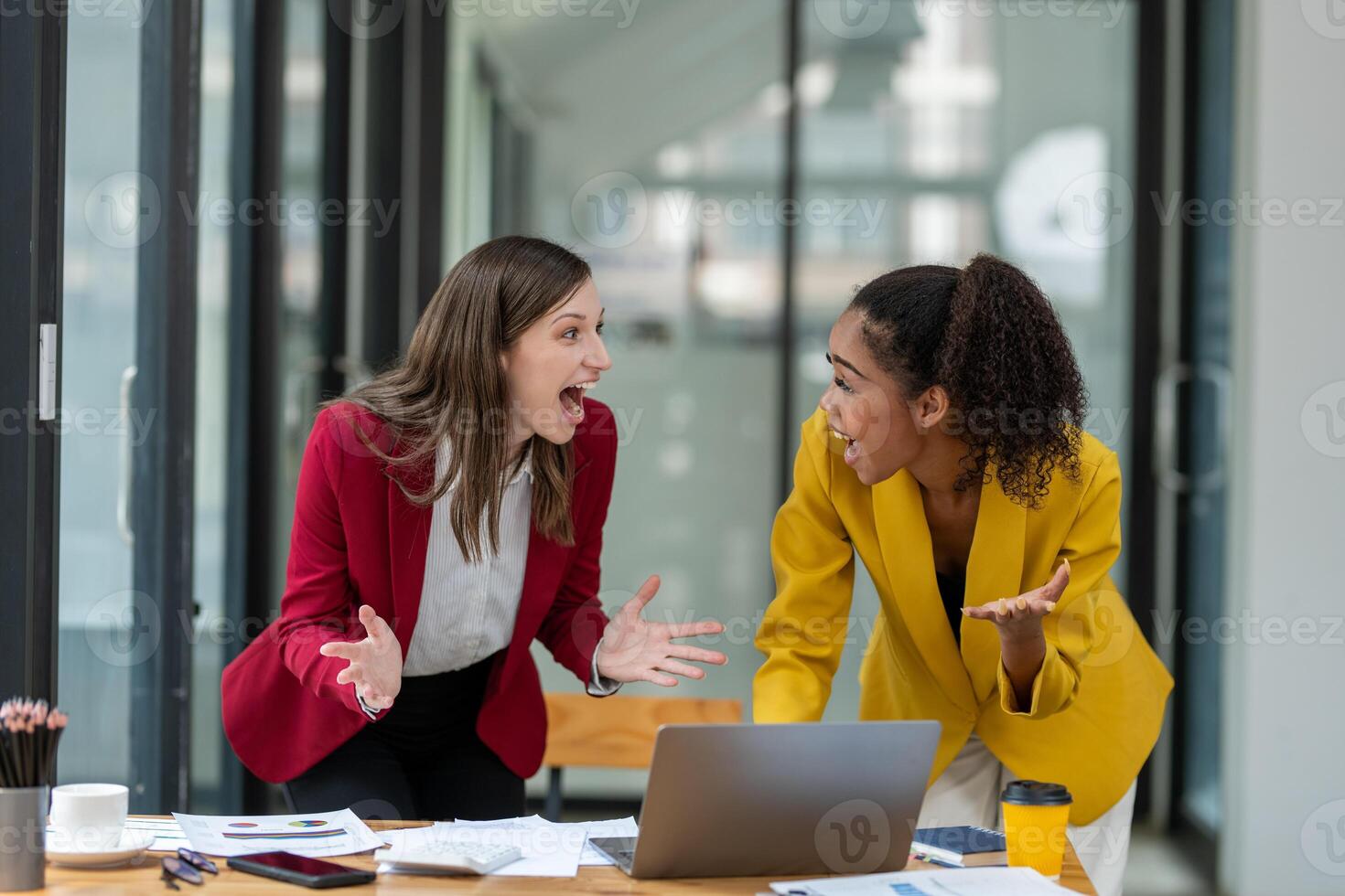 A businesswoman in a yellow blazer engaging in a productive discussion with a colleague in a red jacket over work documents in an office. photo