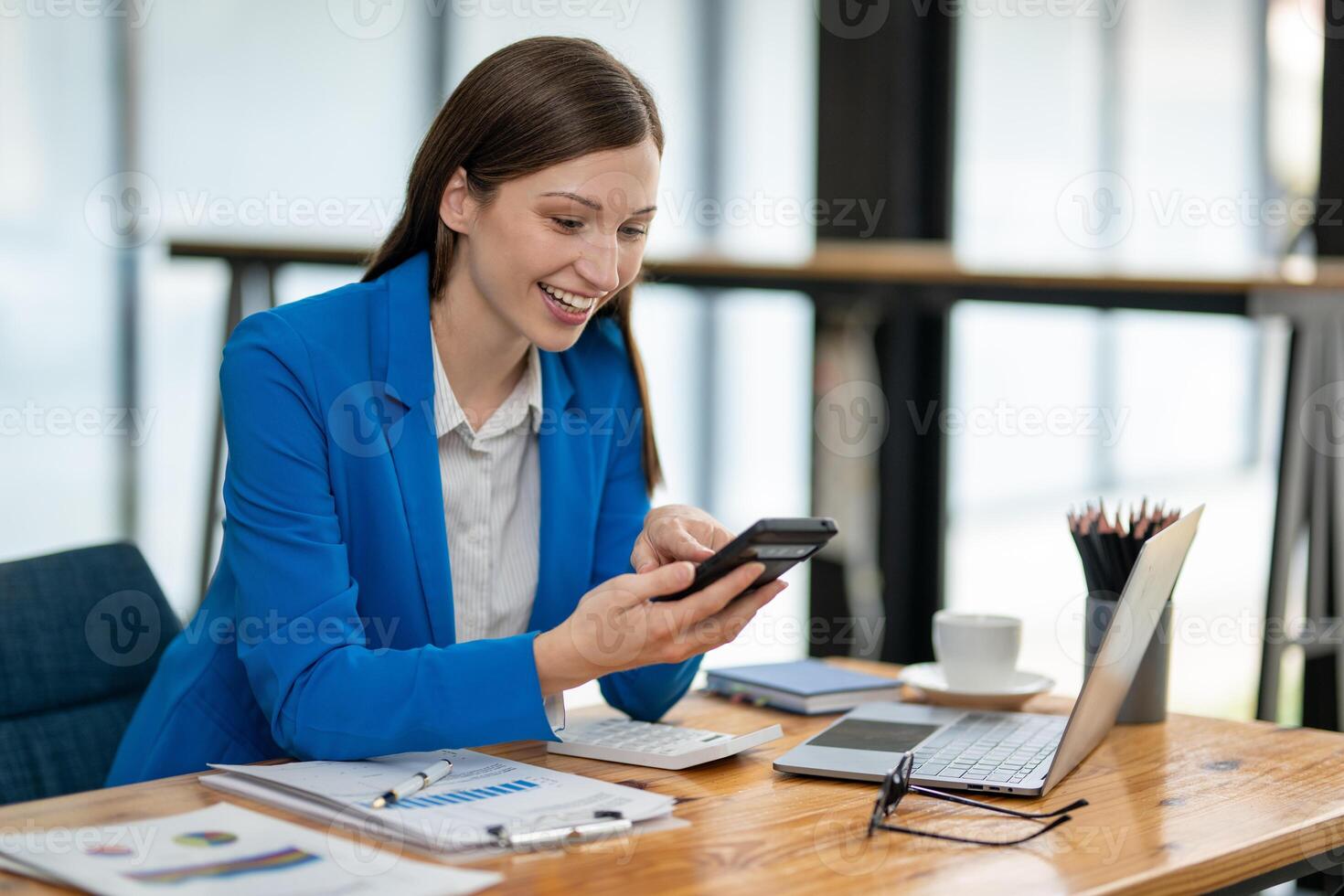 Young professional woman engaged in a phone conversation while working on her laptop at an organized office desk. photo