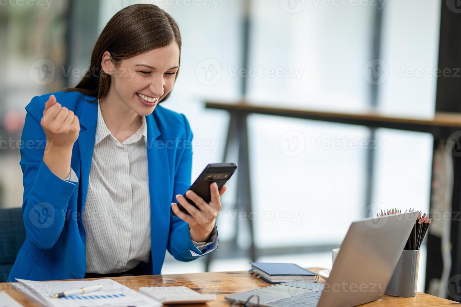 Young professional woman engaged in a phone conversation while working on her laptop at an organized office desk. photo