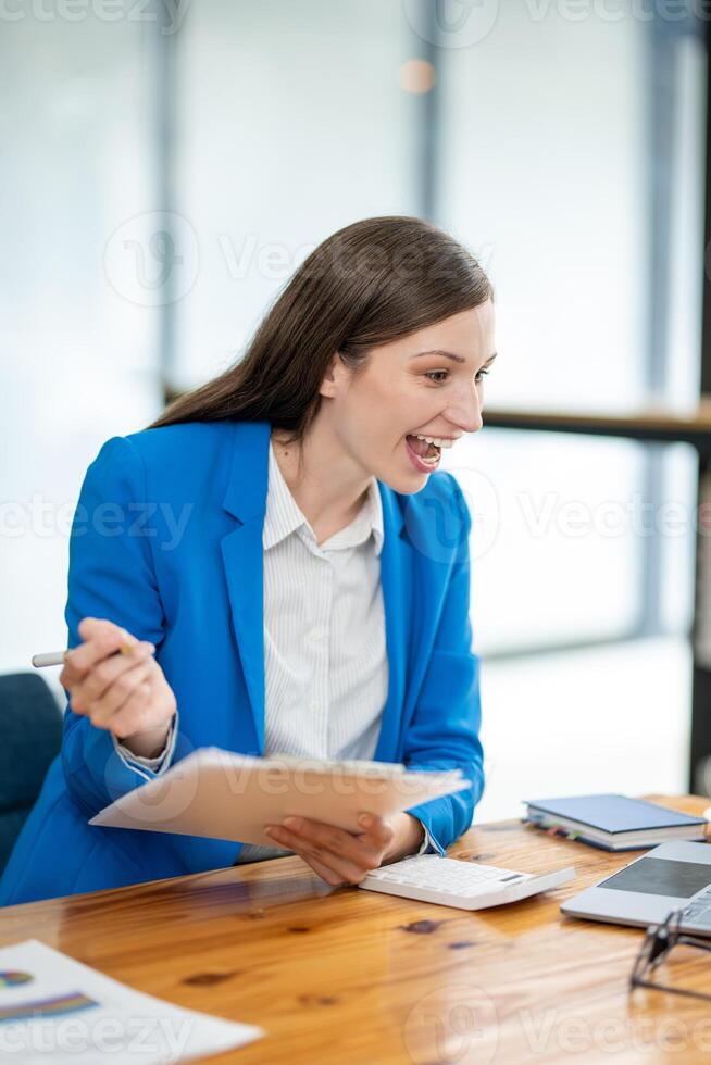Focused young businesswoman analyzing financial reports at a modern workspace with a laptop and office supplies. photo