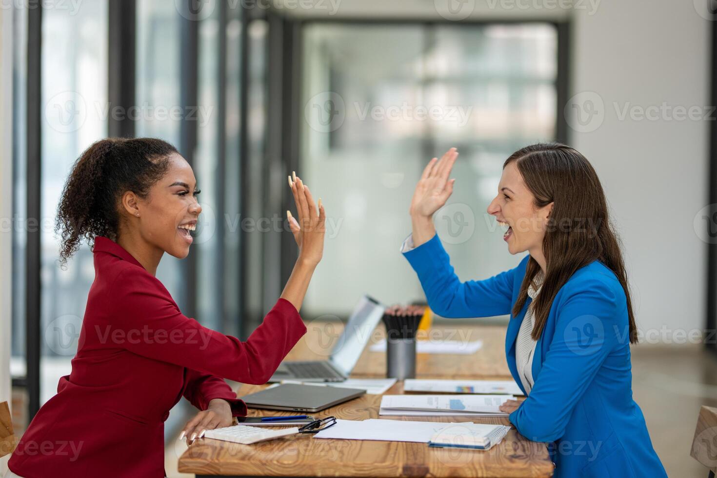 Two happy female coworkers giving a high five, celebrating a successful project or collaboration at their workplace. photo