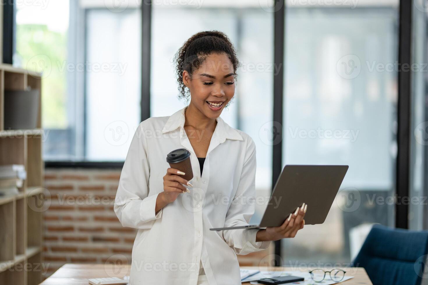A cheerful young businesswoman enjoying a coffee break while working with a digital tablet in a sunny office. photo