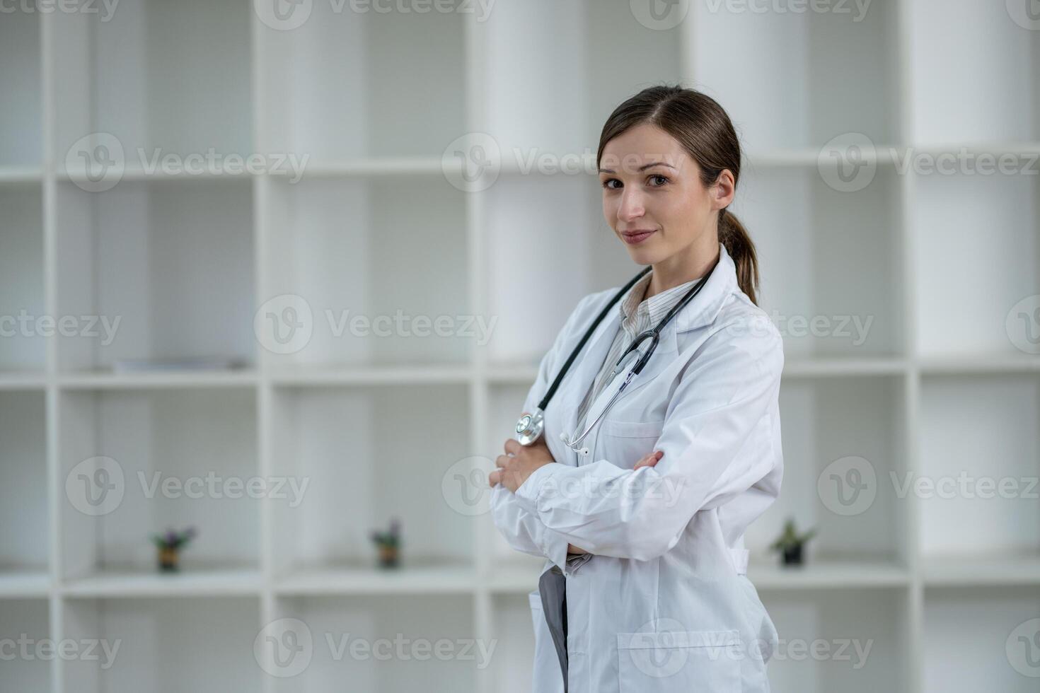 Smiling confident female doctor standing with arms crossed in a white lab coat with a stethoscope, in a clinic's modern setting. photo