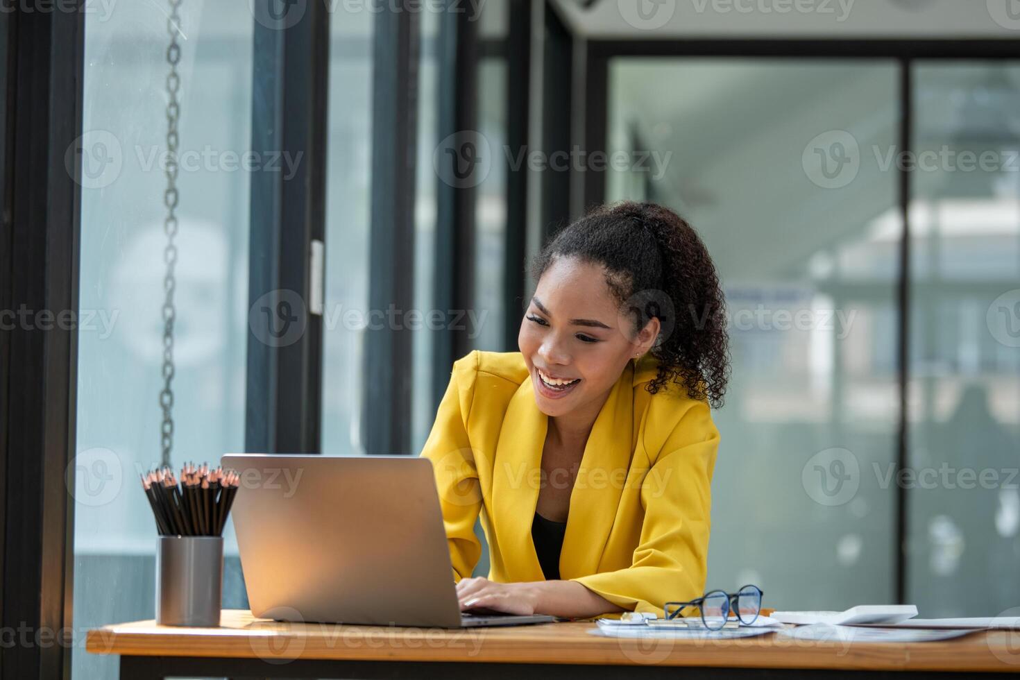 Vibrant businesswoman in a yellow blazer focusing on her laptop screen with excitement in a modern office setting. photo