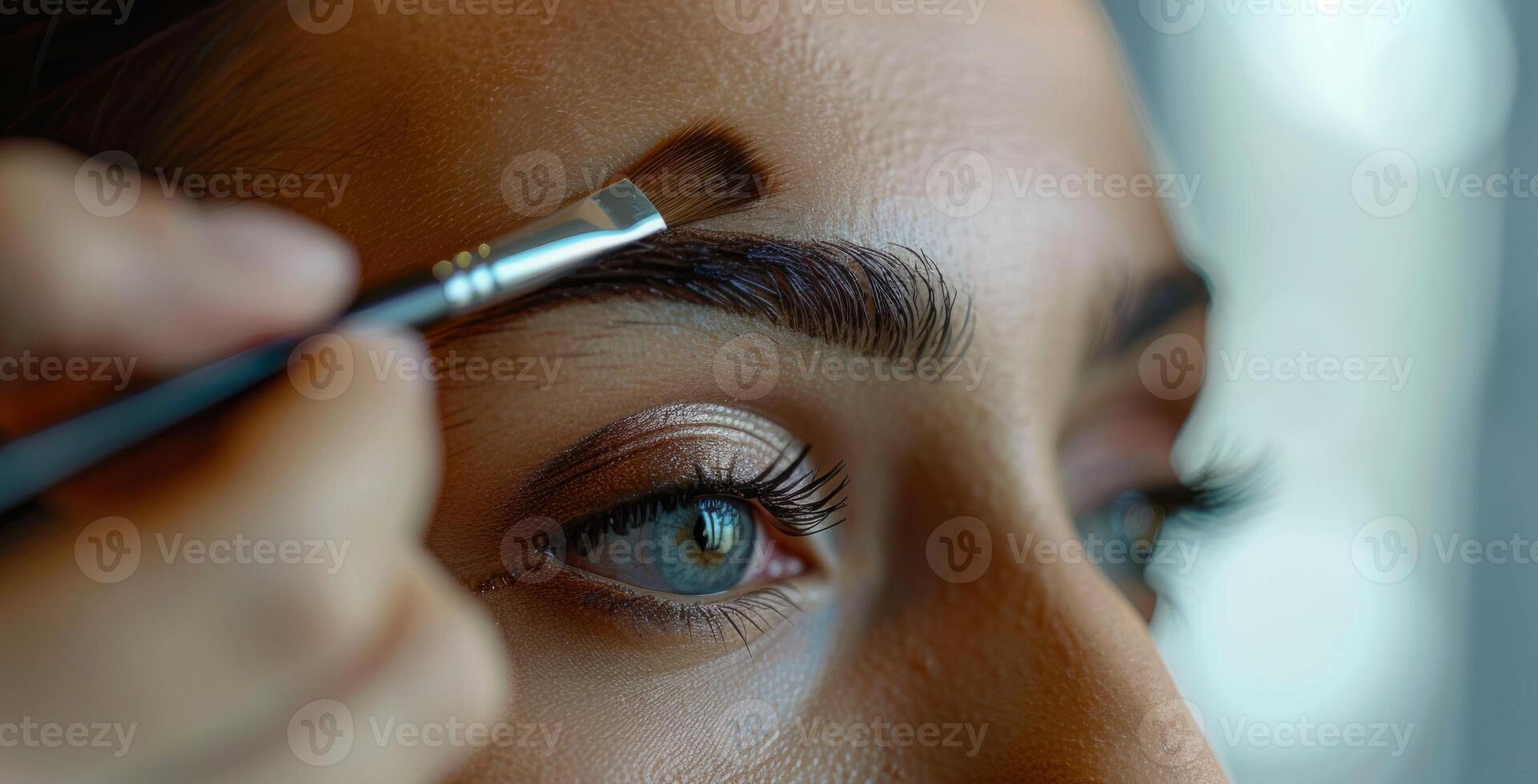 A cosmetologist or makeup artist shapes the eyebrows and tints the client's skin above the eyebrows with a brush, creating a sophisticated look photo