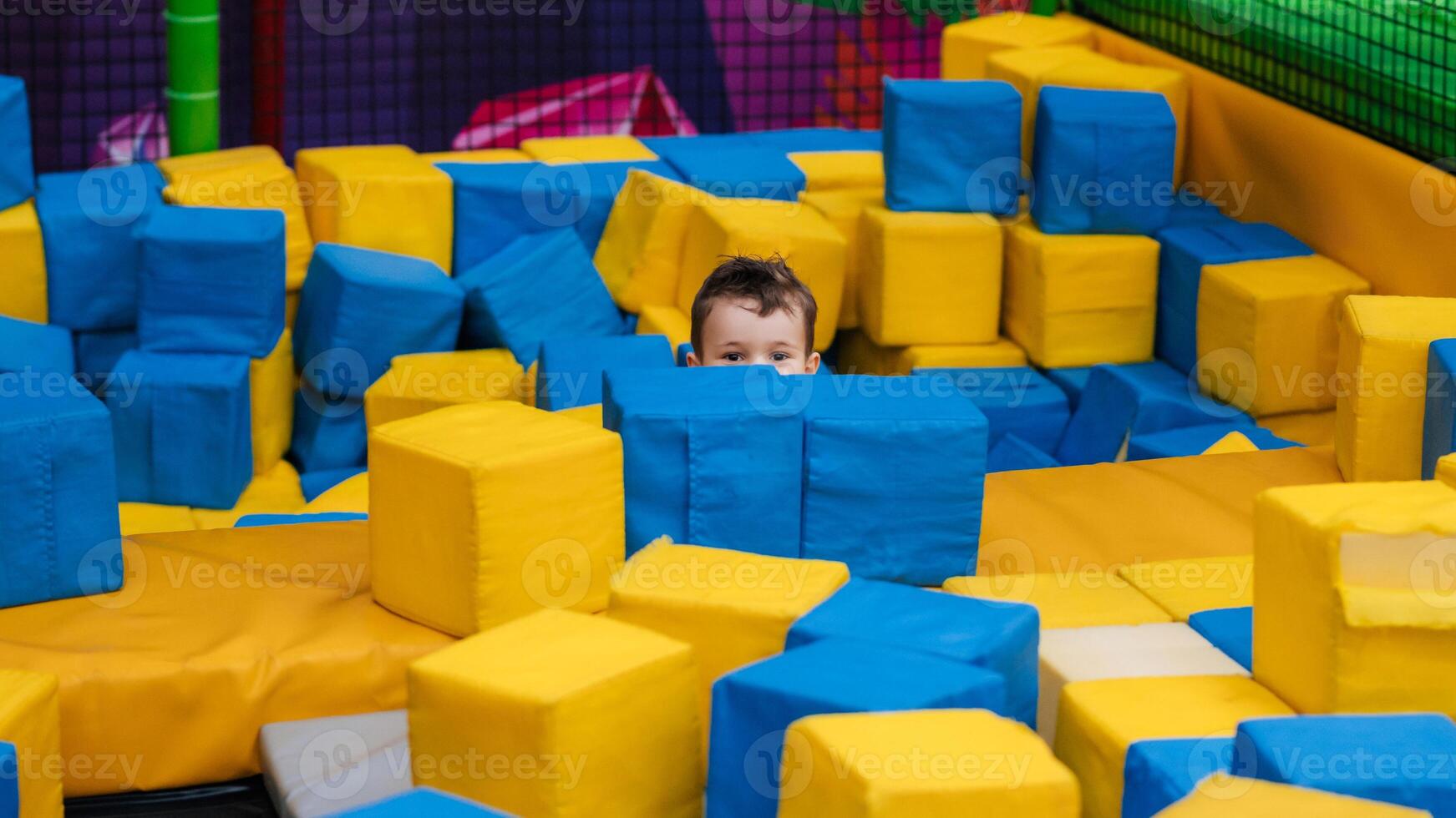 A boy child is playing in a game entertainment nursery. He plays with soft large cubes. Active pastime in the amusement park. photo