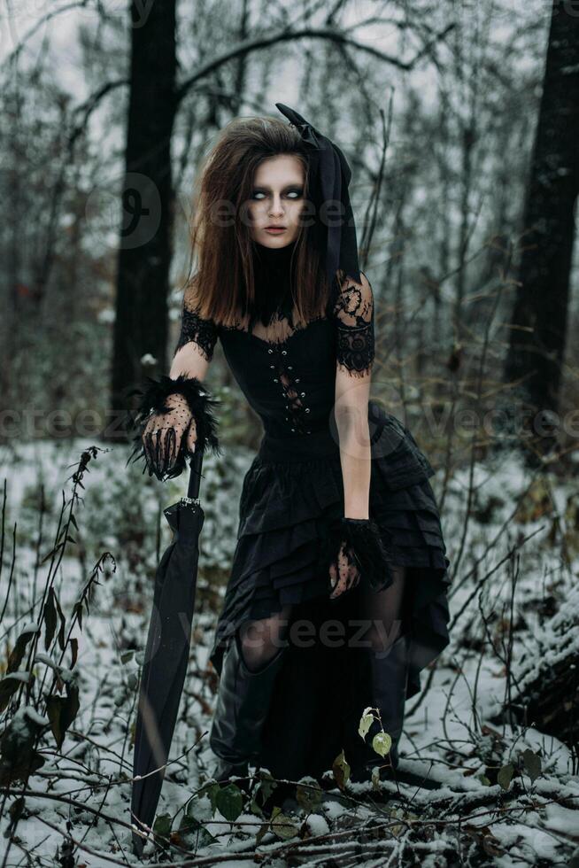 A scary female figure of a witch in a black robe in an autumn forest, an unsaturated image photo