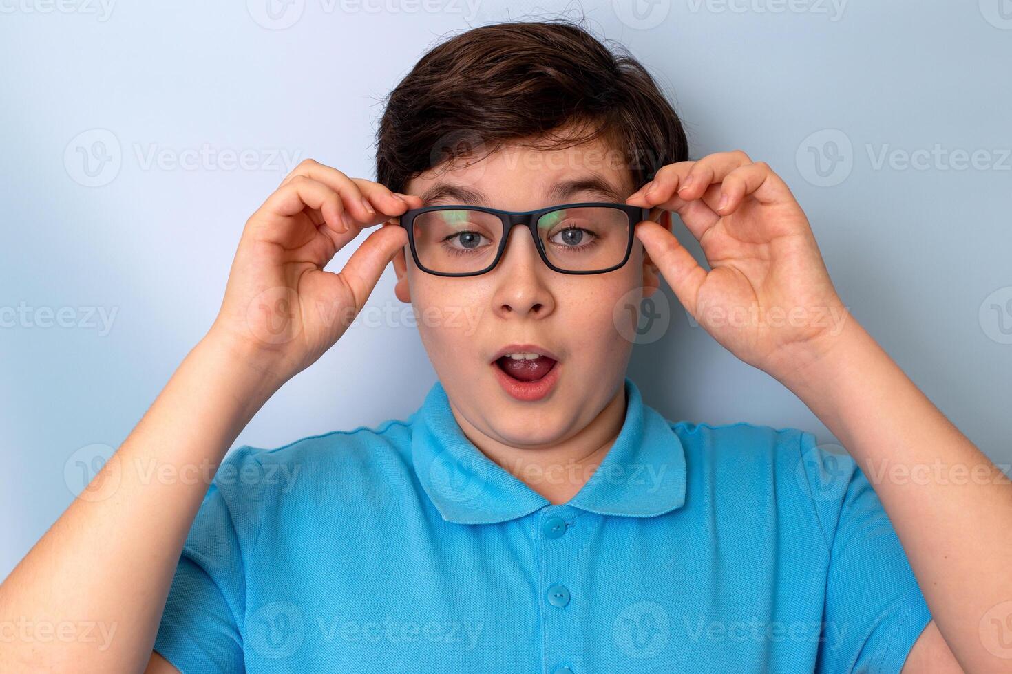 A surprised handsome boy, dark-haired, wearing glasses and a blue T-shirt, photo