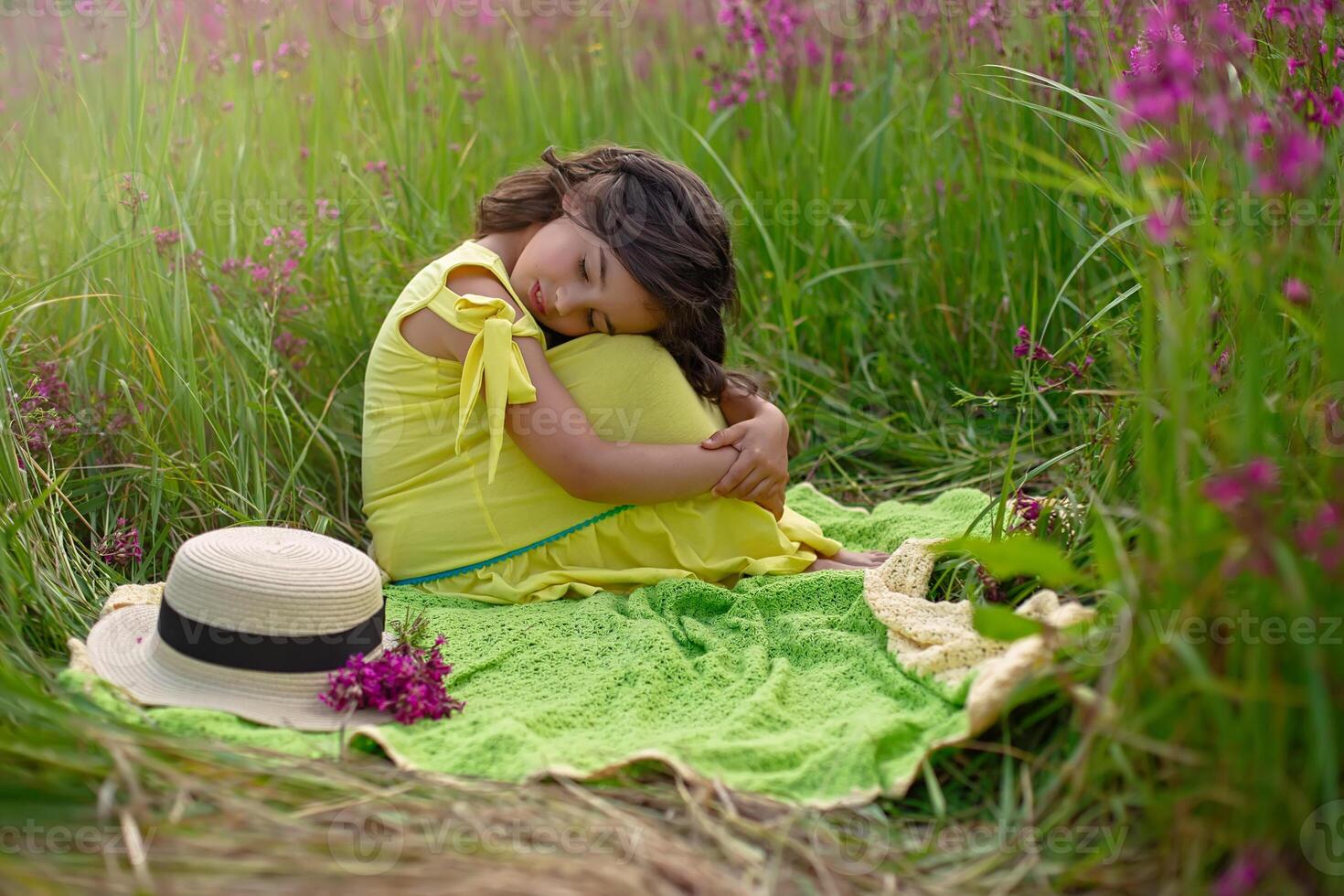 A beautiful little girl, sits hugging her knees and closing her eyes, in a yellow dress photo