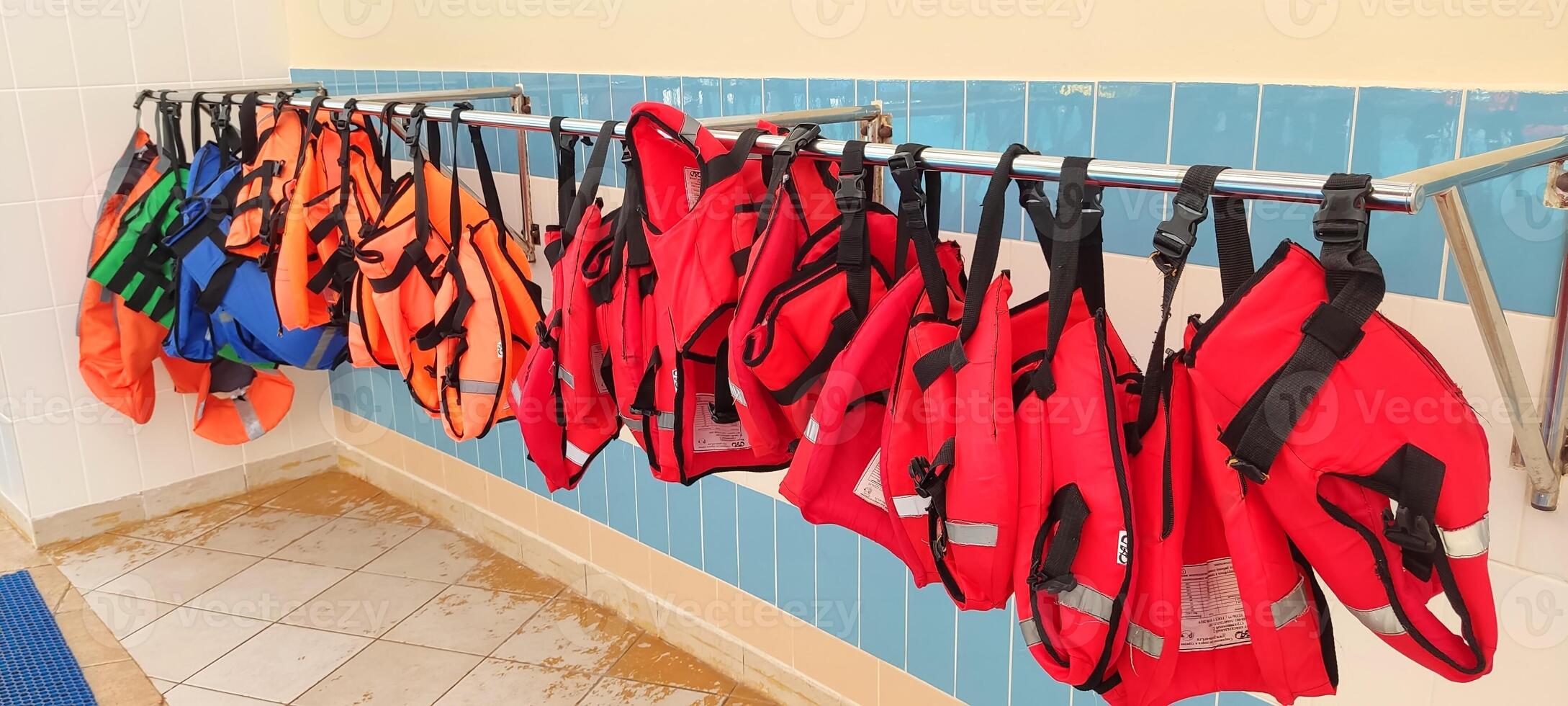 Several red and orange life jackets hang on a hanger, near the gouboi tile wall photo