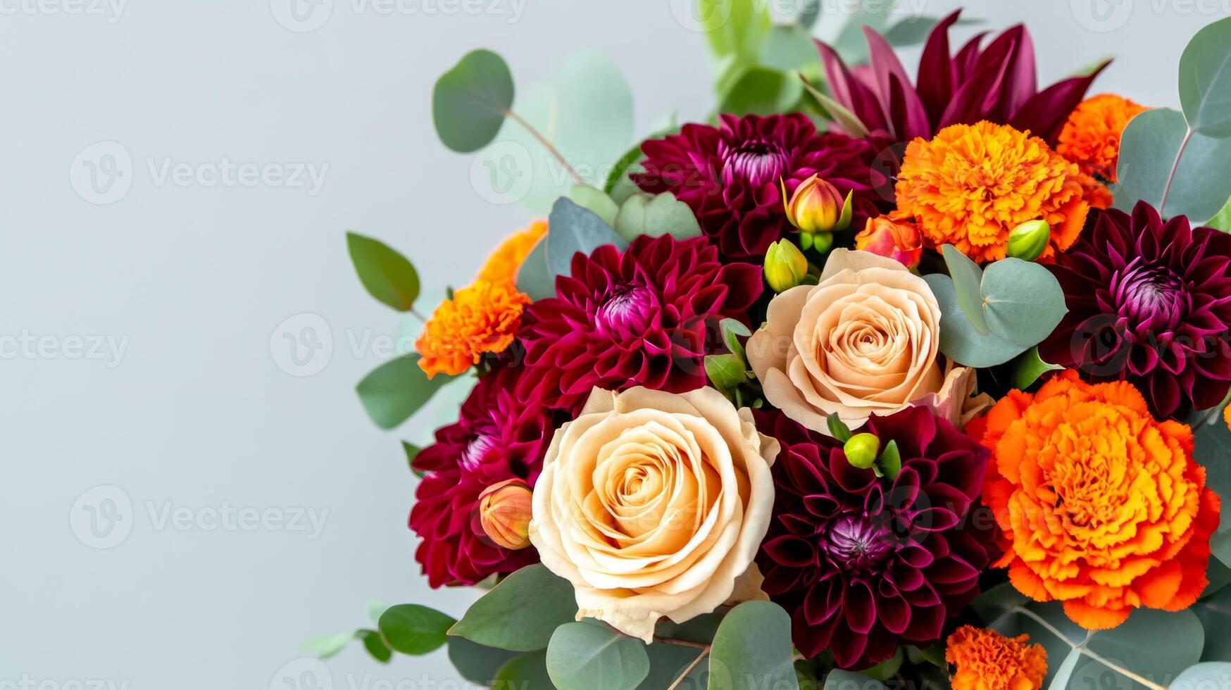 Close up of an elegant autumn bouquet with deep red roses burgundy dahlias and orange marigolds accented with dark green foliage and eucalyptus isolated on a neutral background photo