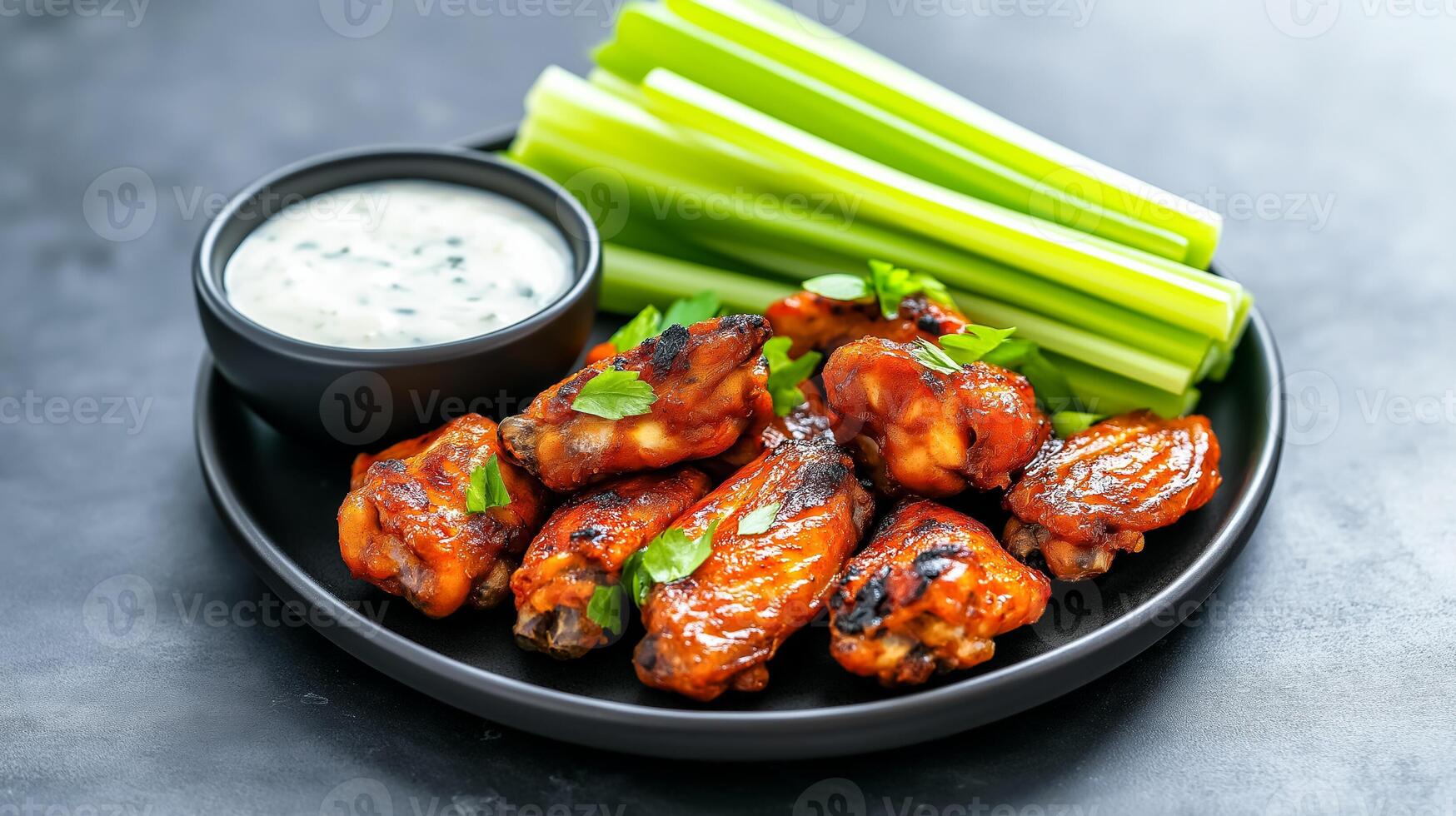Wide shot of ranch sauce being served alongside grilled chicken wings and crunchy celery sticks set on a dark slate plate photo