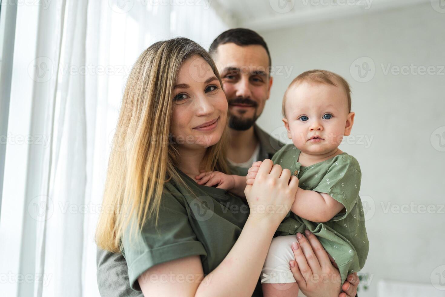 Happy family at home. Mother father holding little toddler child. Mom dad baby girl relax playing having fun together. Woman man hugging embracing baby with love care. Parent of breast feeding baby photo