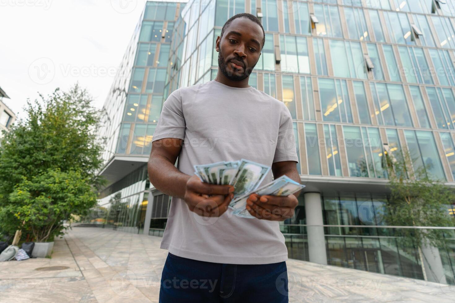 African American man holding money dollar bills on urban street in city. Businessman guy counting paper currency money outdoors near office bank building. Man holding cash. Finance economy banking photo