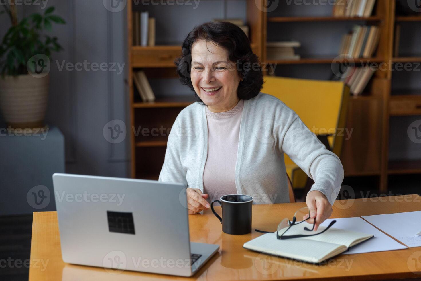 Happy middle aged senior woman sit with laptop talk on call with friends family. Laughing mature old senior grandmother having fun talking speaking with grown up children online photo