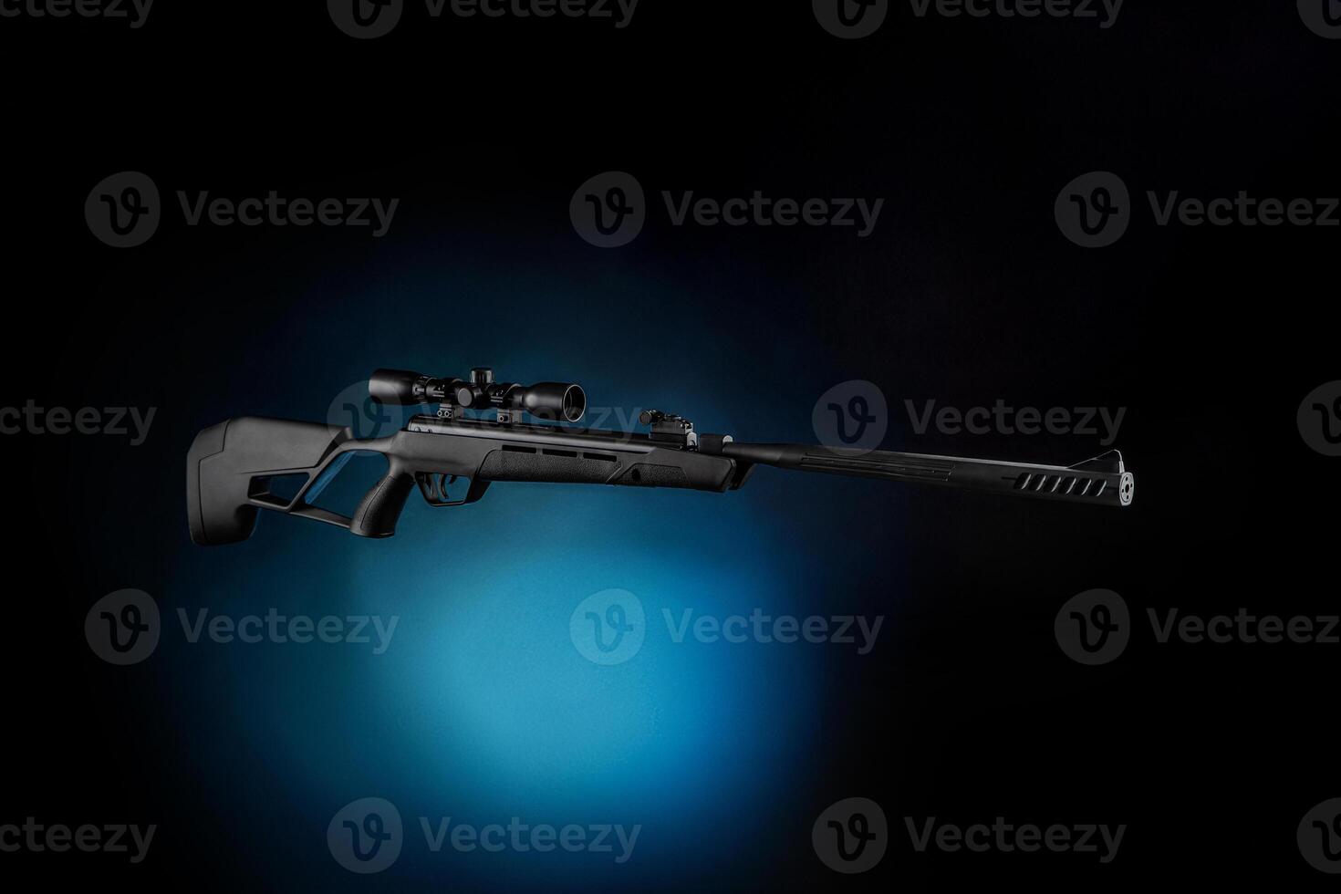 Black pneumatic rifle with an optical sight. Black modern air rifle with a telescopic sight on a dark background. Light blue spot in the back photo