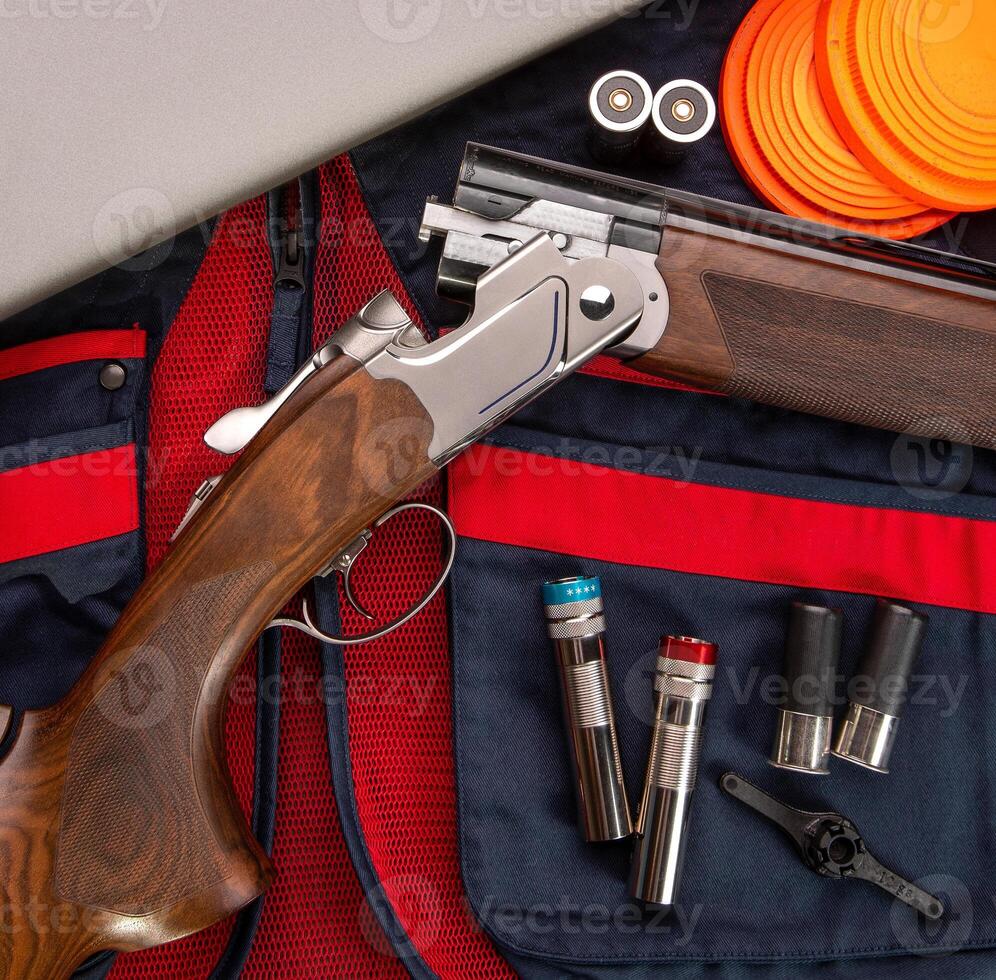 Double-barreled vertical shotgun and cartridges for it on a sports shooting vest. Shooting sport poster concept. Clay target plates for shooting with rifle on wooden back photo