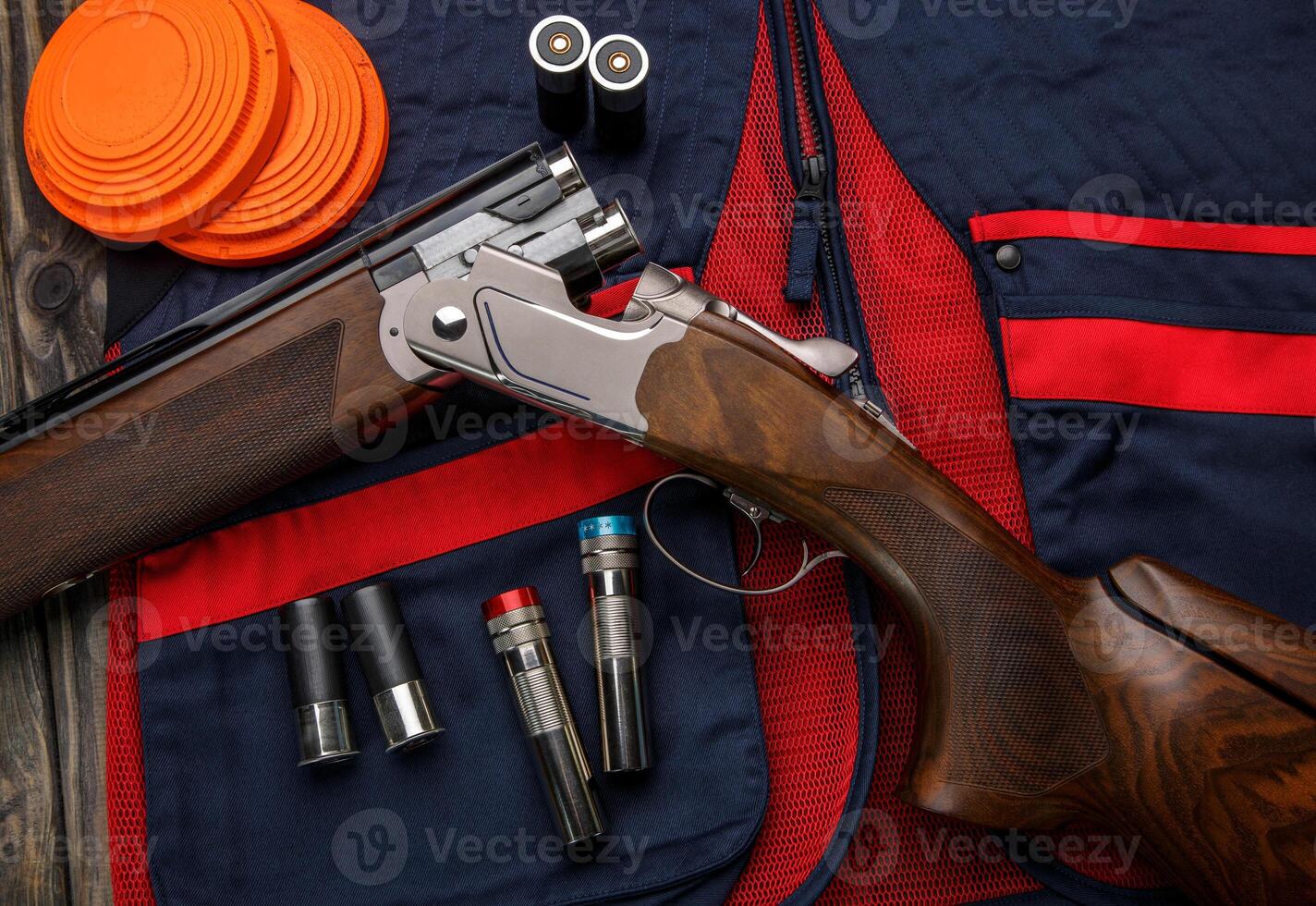 Double-barreled vertical shotgun and cartridges for it on a sports shooting vest. Shooting sport poster concept. Clay target plates for shooting with rifle on wooden back photo