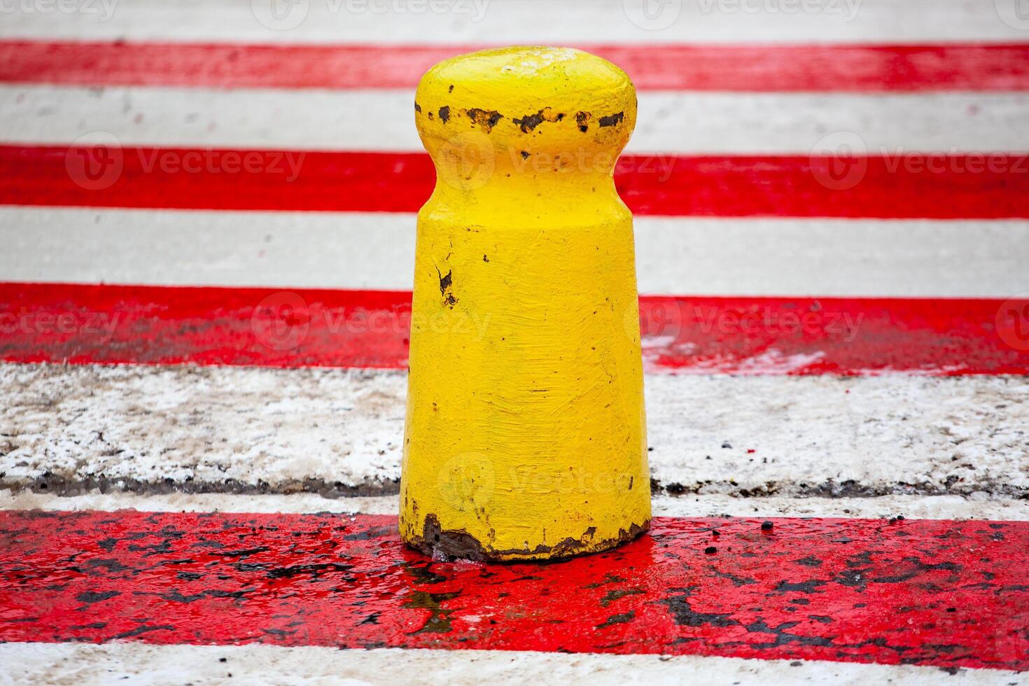 Yellow concrete post on a red and white crosswalk. Parking barrier photo