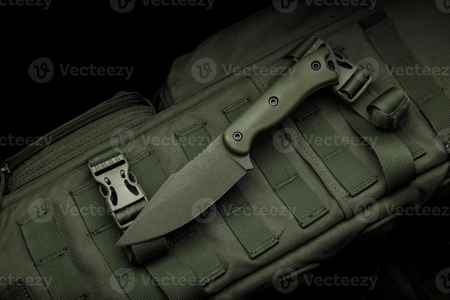A modern military knife and a plastic sheath for it. Edged weapons lie on a military olive-colored backpack. photo