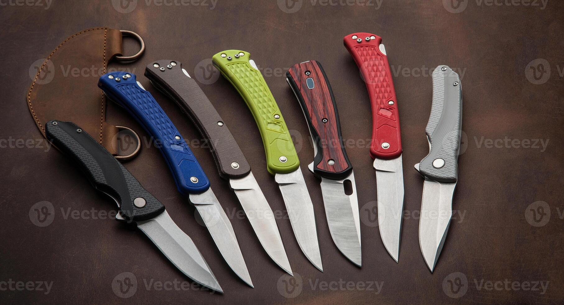 Multi-colored penknives on a brown leather background. Different folding knives lie on a large piece of brown leather. photo