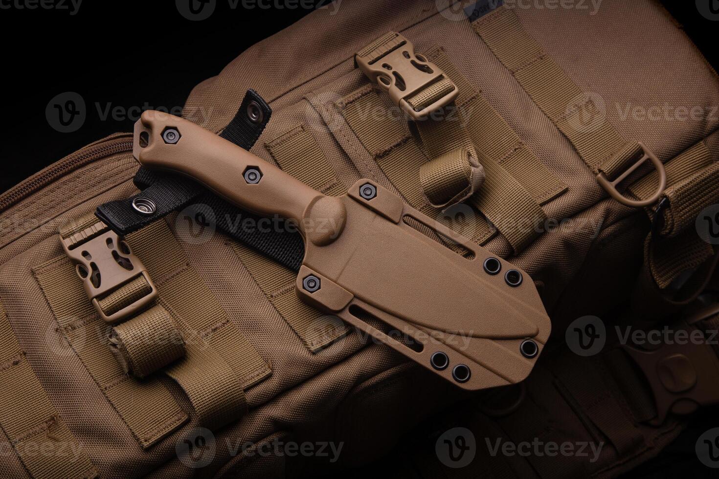 A modern military knife and a plastic sheath for it. Edged weapons lie on a desert-colored military backpack. photo