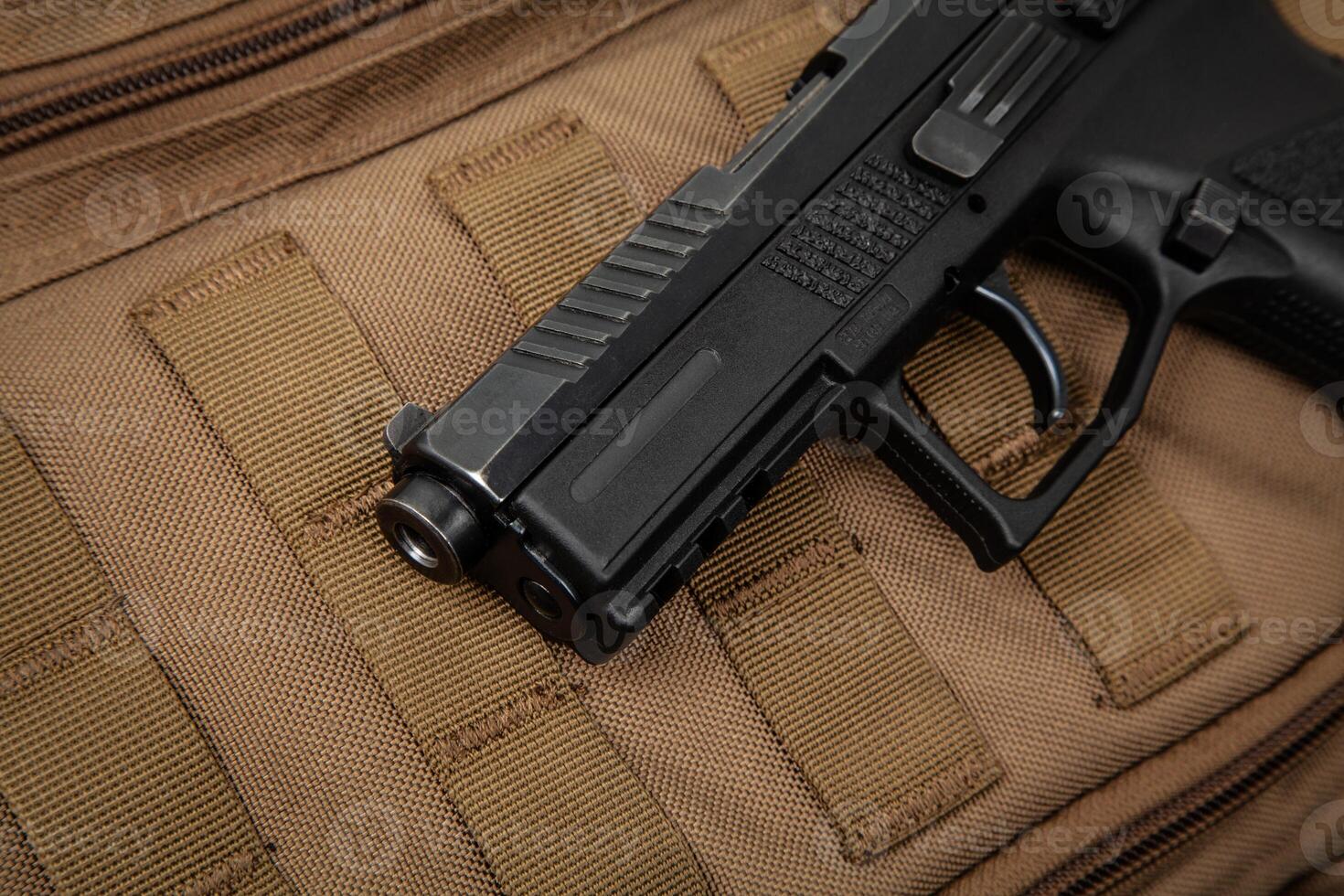 A modern black pistol on a brown military backpack. Weapons for defense and attack. Arming the police, army and special units photo
