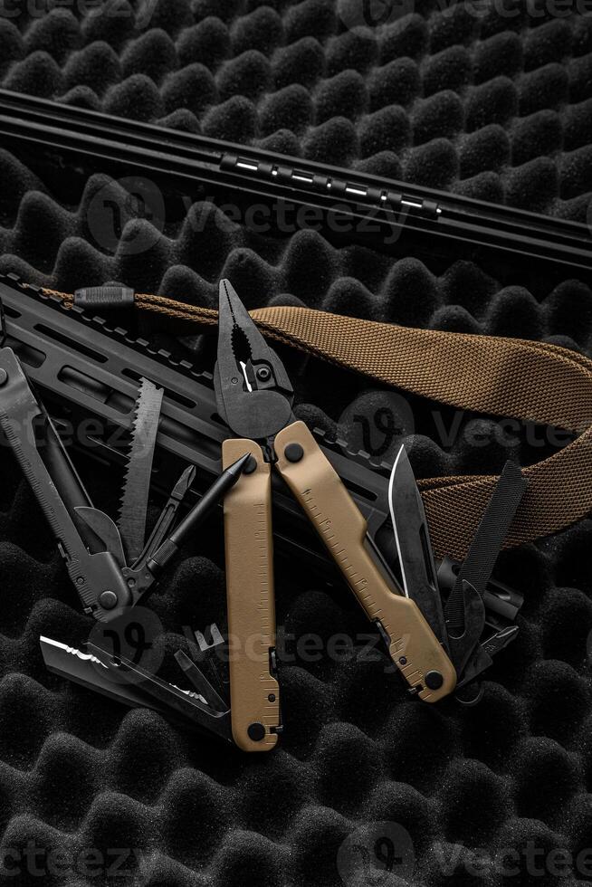 Modern multitool with many tools. A portable multi-tasking military tool lies next to the weapon. Dark back. photo