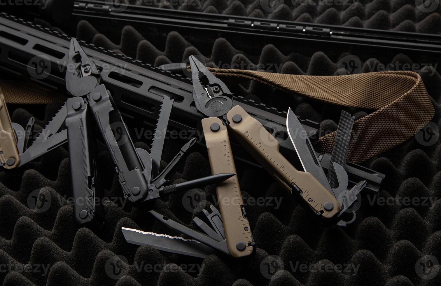Modern multitool with many tools. A portable multi-tasking military tool lies next to the weapon. Dark back. photo