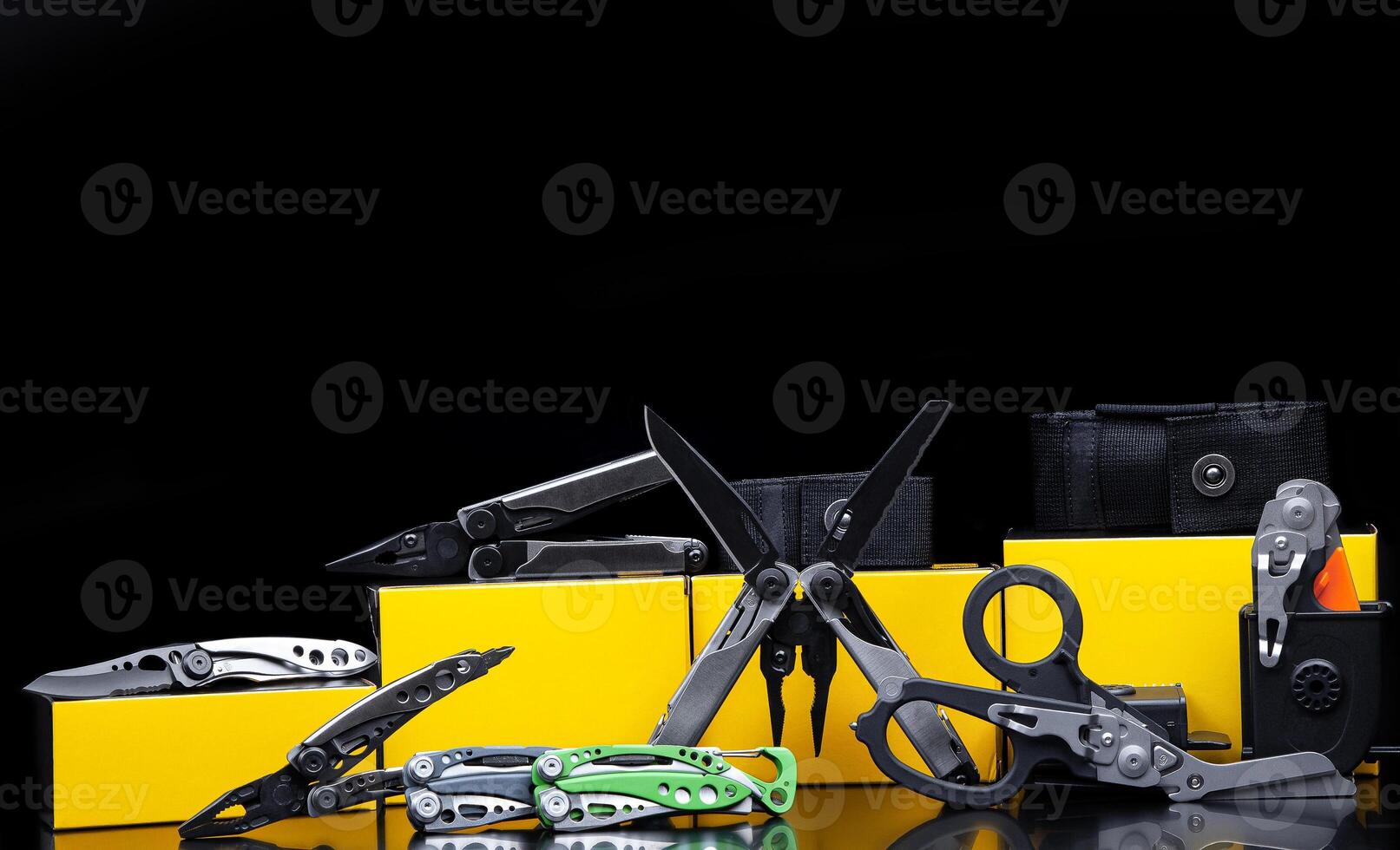 A variety of multi-tool knives and scissors on a glossy surface. Cases and boxes for them. Dark back. photo