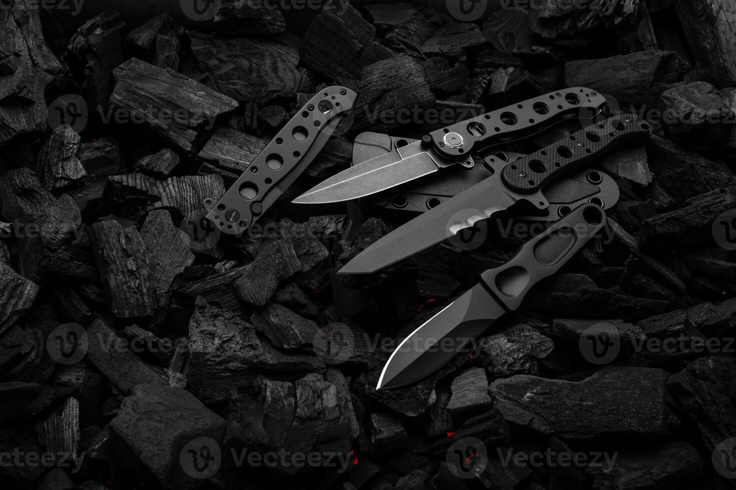 Modern knives with black blades. Hunting, military and folding knives on smoldering charcoal. Black back. photo