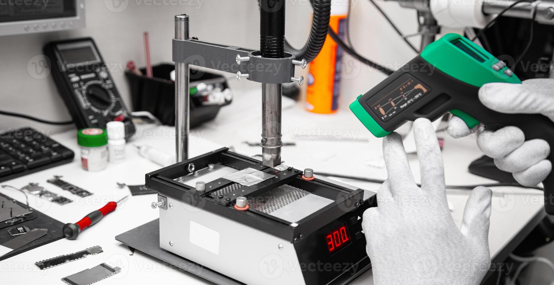 The master measures the temperature of the microchip at the soldering station with a laser thermometer. Service center. Repair of microelectronics. photo