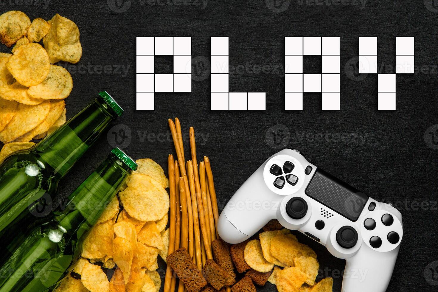 Modern white gamepad among chips, crackers and bottles of beer on a black. Game concept. photo