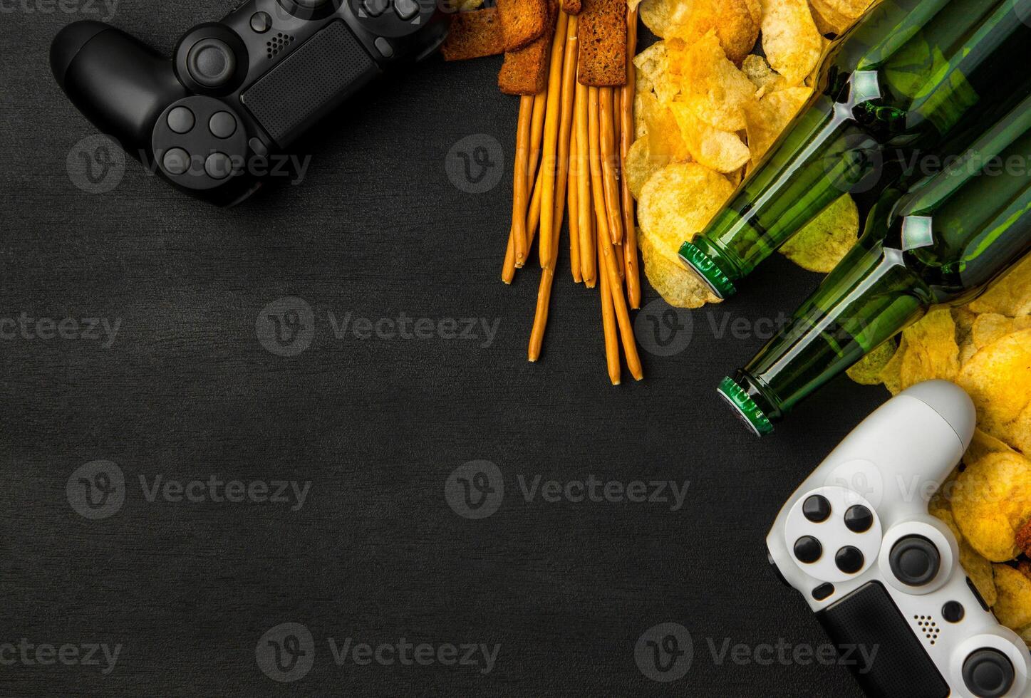 Modern white gamepad among chips, crackers and bottles of beer on a black. Game concept. photo