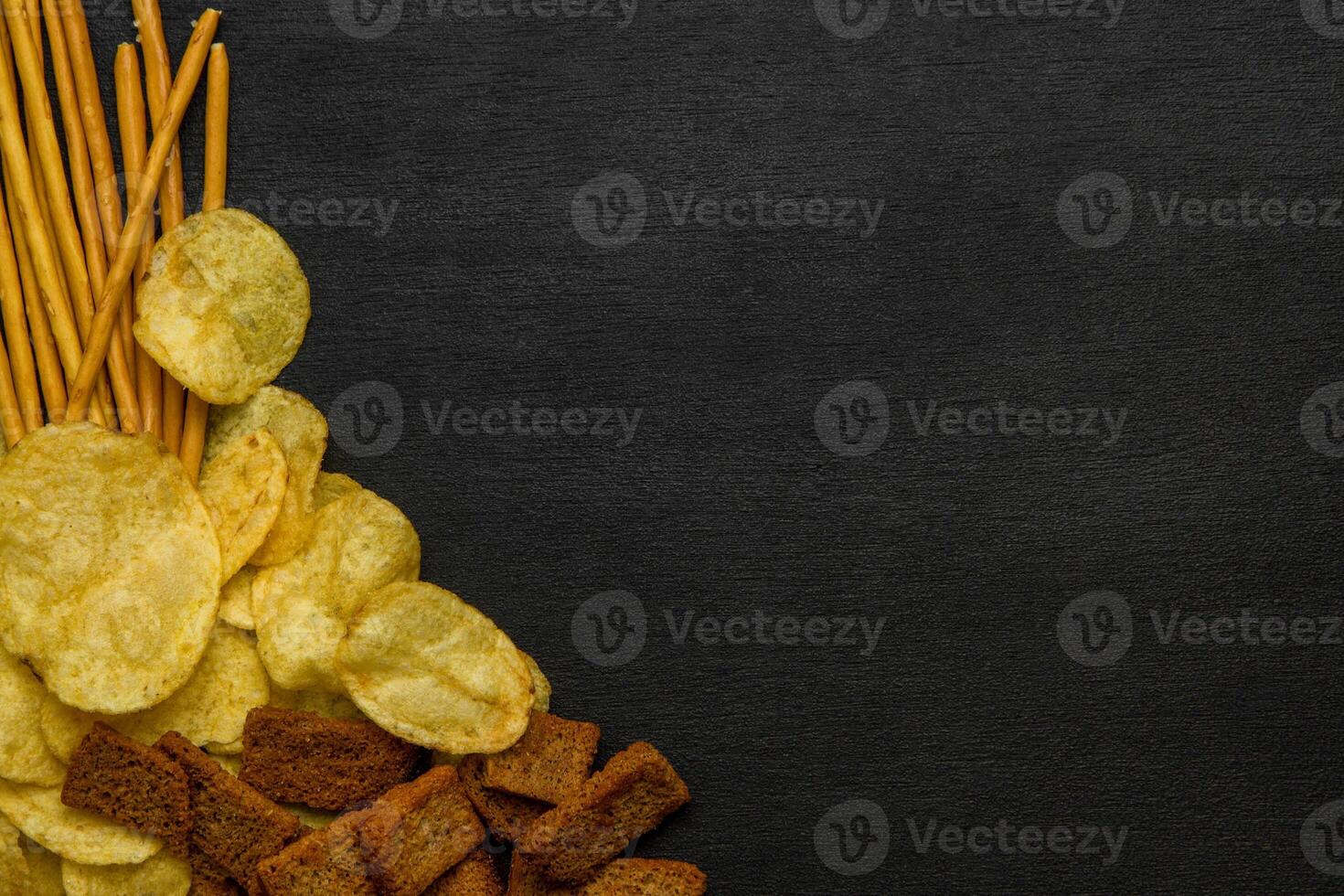 Crisps, crackers and salty pretzel sticks on a dark background. Beer snacks. photo