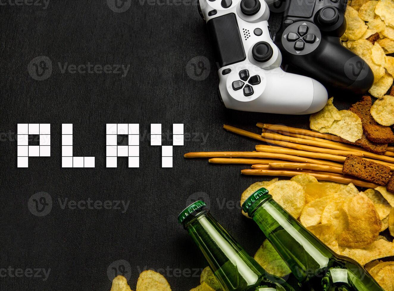 Modern white gamepad among chips, crackers and bottles of beer on a black. Game concept. photo