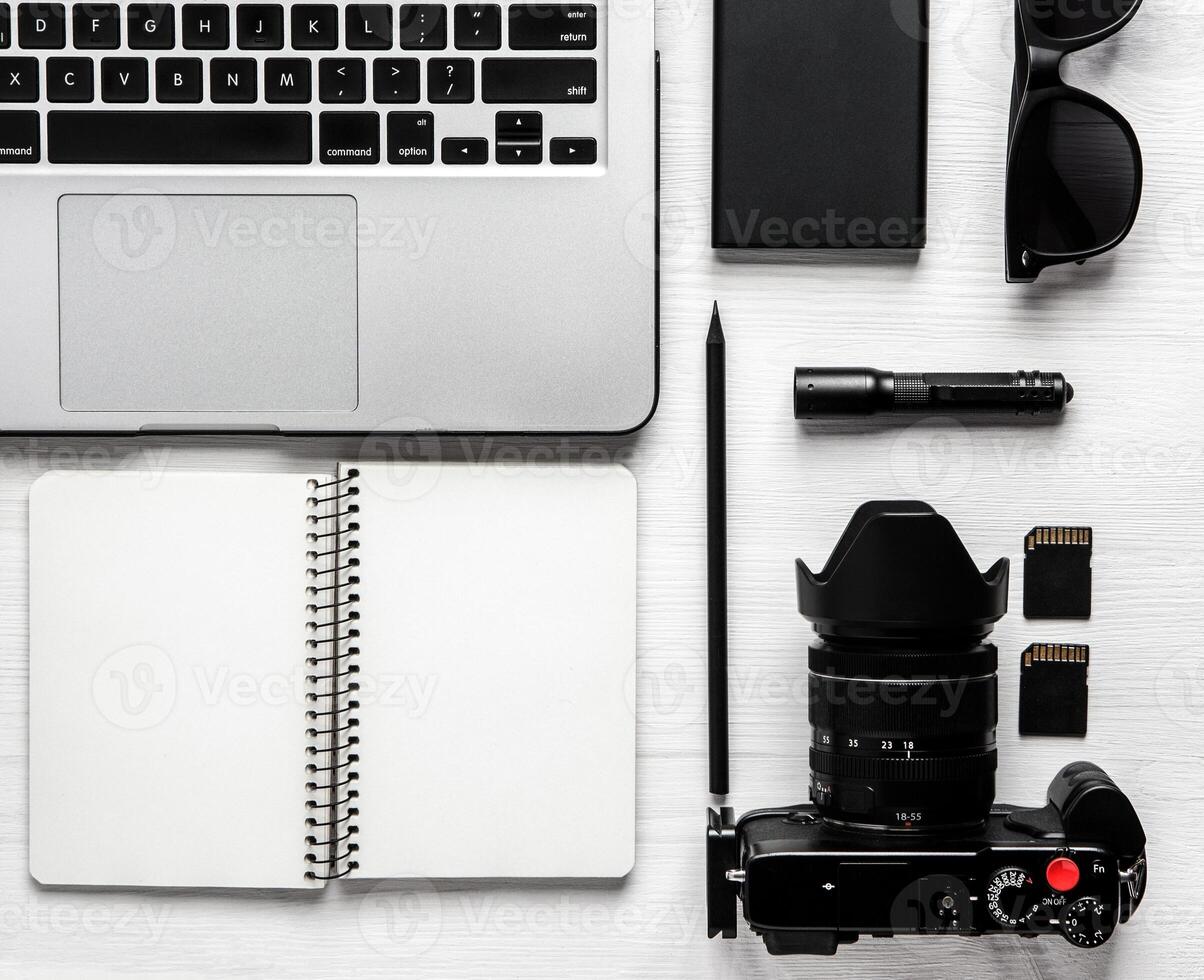 Notebook, laptop, photo camera and flashlight and glasses on a white wooden background.